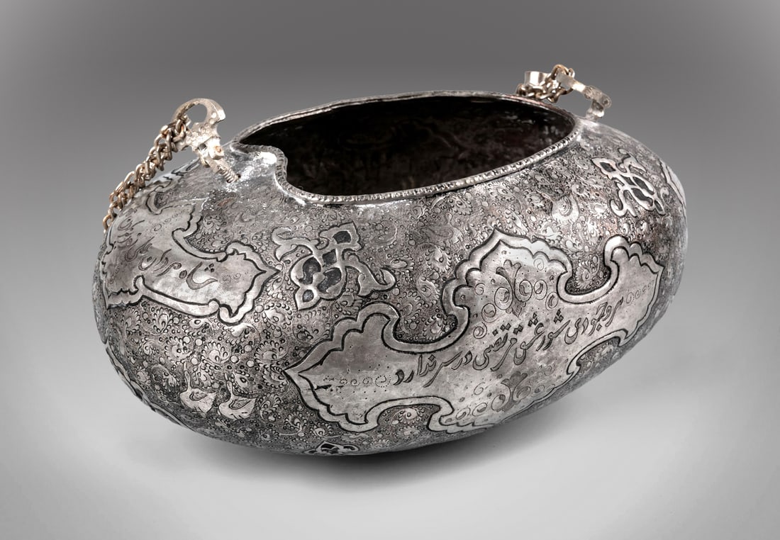 An Impressive Tin-Plated Copper Qashkul, Persia, 19th Century: An Impressive Tin-Plated Copper Qashkul, Persia, 19th Century Oval form with two large medallions bearing Arabic calligraphy engraved on either side. The underside features three medallions depicting