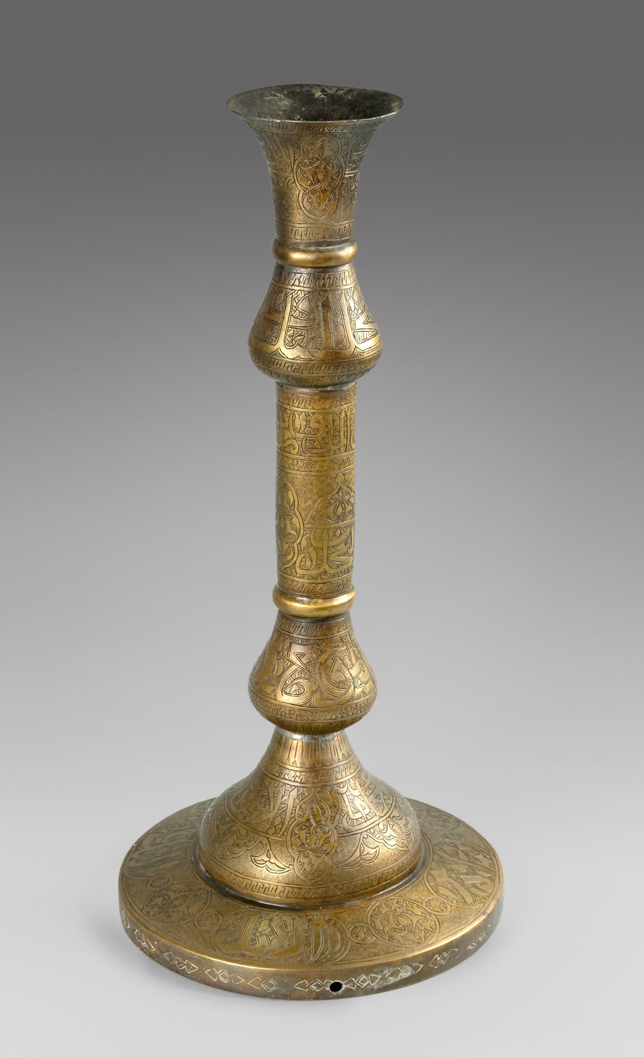 A Large Islamic Brass Candlestick, 19th Century: A Large Islamic Brass Candlestick, 19th Century Raised on a wide circular base, the surface is finely engraved throughout with floral ornament and centered inscriptions in Arabic calligraphy. Well pr