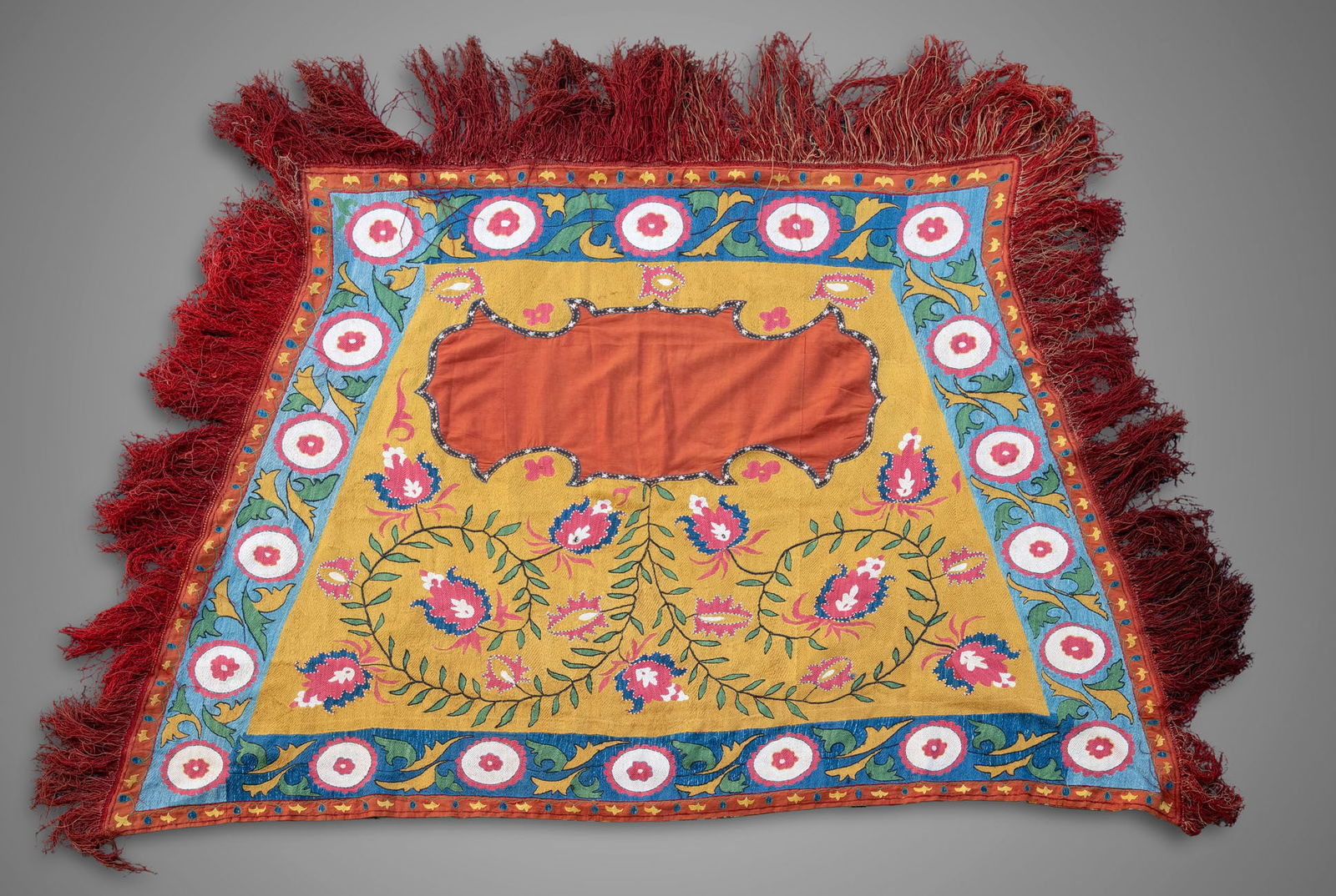A Lakai Suzani Saddle Cover Textile, Late 19th Century: A Lakai Suzani Saddle Cover Textile, Late 19th Century Embroidered with multicolored floral motifs and finished with matching fringe. The reverse is lined in ikat-dyed fabric in orange tones. Triangu