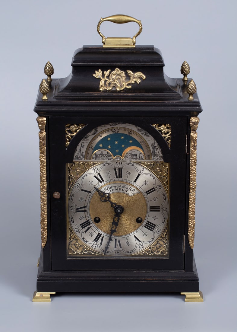 A Thomas Smith Ebonized Wood and Gilt Brass Ormolu Table Clock, England, Early 20th Century: A Thomas Smith Ebonized Wood and Gilt Brass Ormolu Table Clock, England, Early 20th Century Housed in a rectangular, ebonized wood case fitted with a hinged glass door and raised on four gilt-brass su