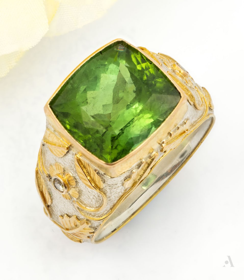 A Silver and 18K Yellow Gold Tourmaline and Diamond Ring: A Silver and 18K Yellow Gold Tourmaline and Diamond Ring Centered by a green tourmaline (approx. 13.8 x 12.8 mm), set in a gold bezel. The band is fashioned in sterling silver, decorated with hand-eng