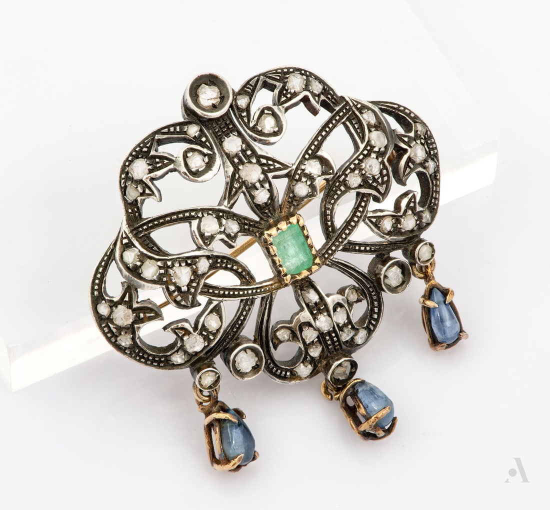 A Silver Gold Diamond Emerald and Sapphire Brooch: A Silver Gold Diamond Emerald and Sapphire Brooch Designed in an elaborate openwork foliate motif, centering upon a rectangular step-cut emerald. The mount accented throughout with rose-cut diamonds a