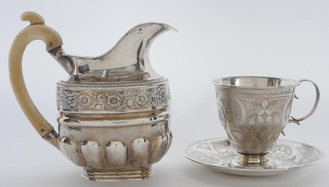 2 piece Russian Silver Table Items: 2 piece total to inlcude 1) Embossed open creamer, bone handle, marked with Cyrillic D.Sh., possible Dmitry Shelaputin, 1830 assay mark. 5" h .x 5.25". 2) Engraved teacup and saucer, unknown maker Cyr