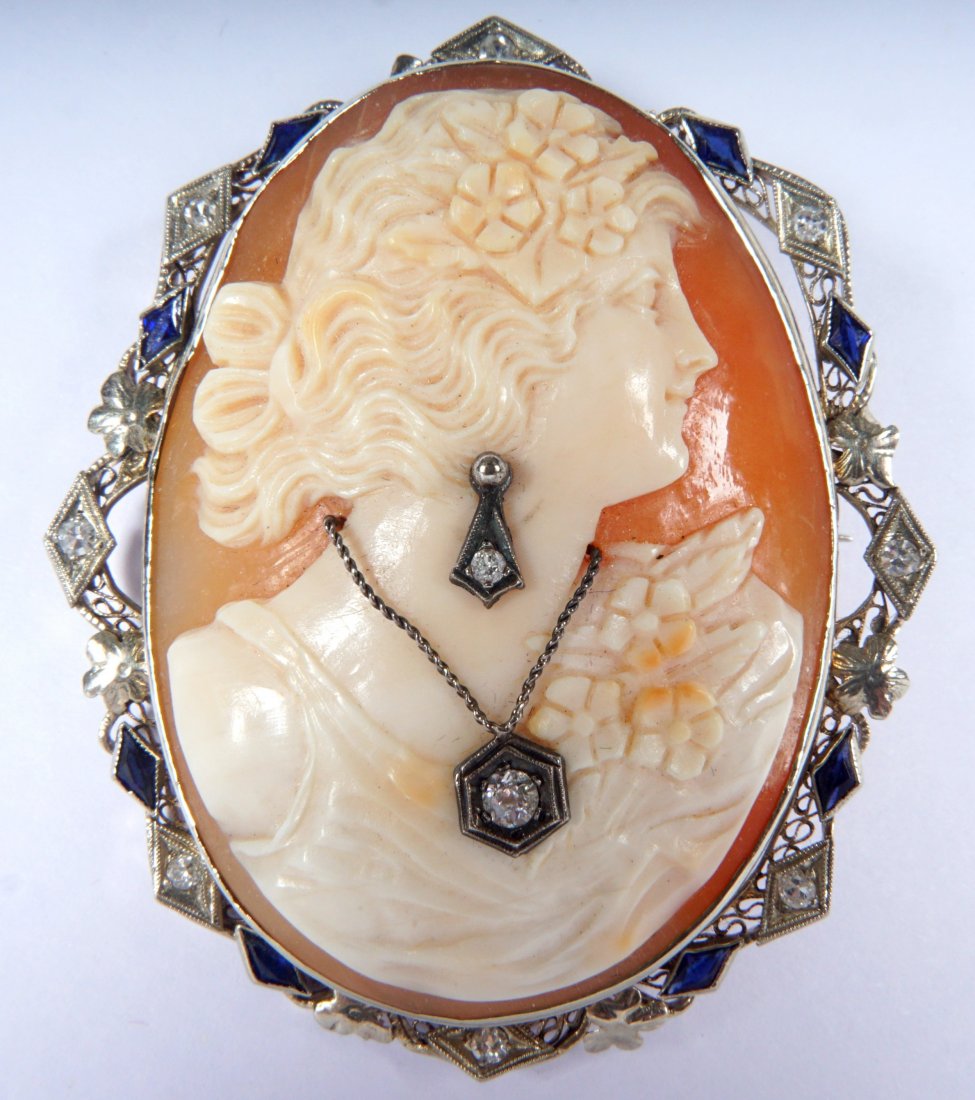 14K CALIBRATED SAPPHIRES & DIAMOND CAMEO BROOCH: Oval shape with female profile wearing a diamond drop earring and pendant surrounded by a perimeter of diamonds, calibrated sapphires and floral accents in white gold. 2" L x 1-3/4" W.
