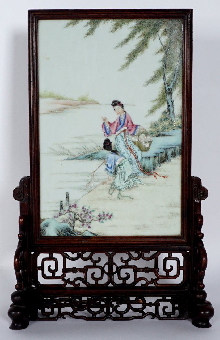 Chinese Famille Rose Porcelain Plaque Table Screen: Porcelain plaque with outdoor genre scene of 2 women at the bank of a river washing silk ribbons, no visible signature, sight size 14.5" x 9.5". Pierced carved wood base, 10" x 13.75" x 5.75". Conditi