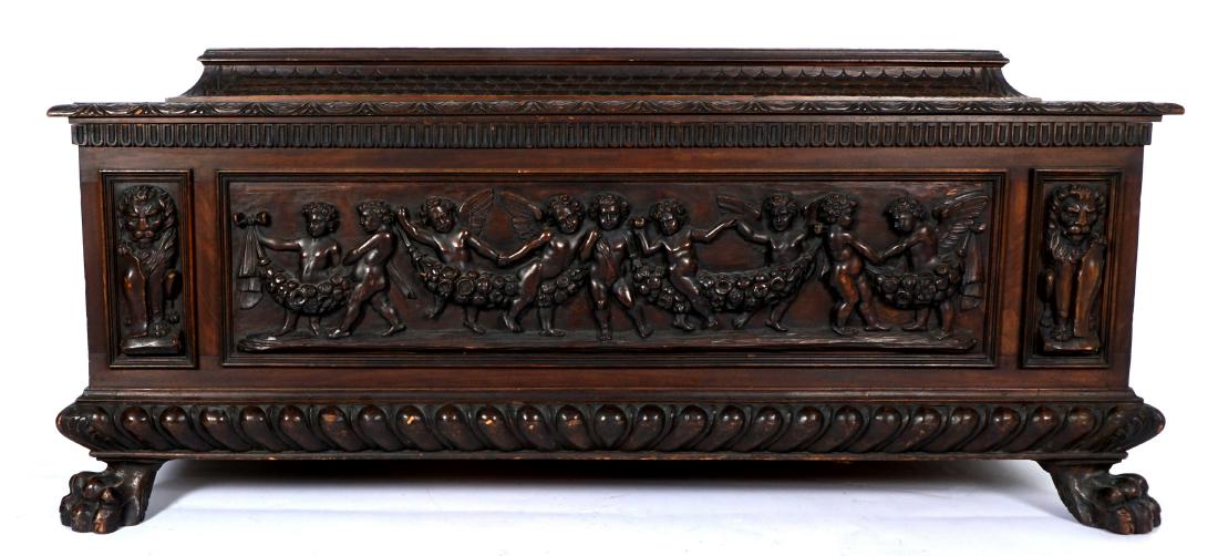 19th Century Italian Carved Walnut Cassone: Baroque style cassone, stepped top with fish scale shaped sides, carved trim hinged lid. Front with relief carved cherubs, putti, and foliate garland, flanked either side with figural lions with shiel