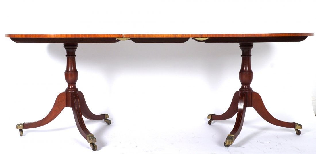 Duncan Phyfe Style Double Pedestal Dining Table: Banded mahogany to with oval ends, turned double pedestal base, flared tripod legs, brass claw feet ending in castors. 28.75" h. x 66" x 39", sold with single 18" leaf. Condition: Typical scratches to
