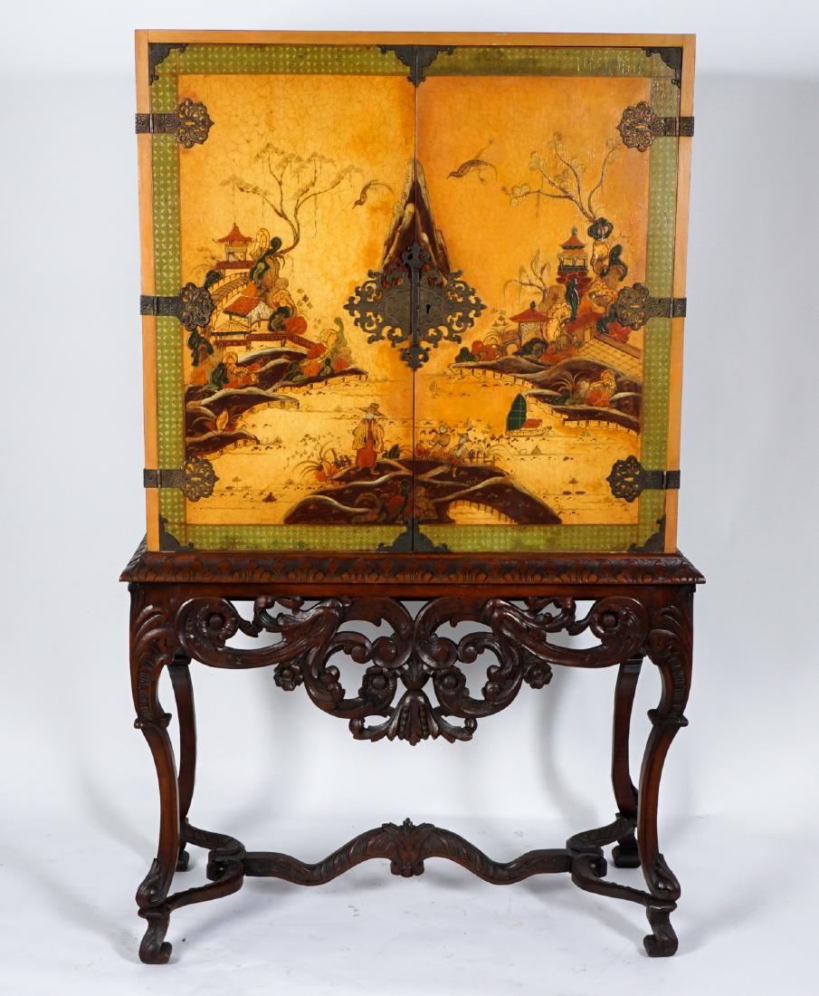 Chinoiserie Cabinet on Stand: Polychrome chinoiserie decorated chest, 2 door front with outdoor genre scene, painted interior with 2 shelves. Carved stand with openwork foliate scroll skirt, shaped legs and stretcher. Overall 64.5