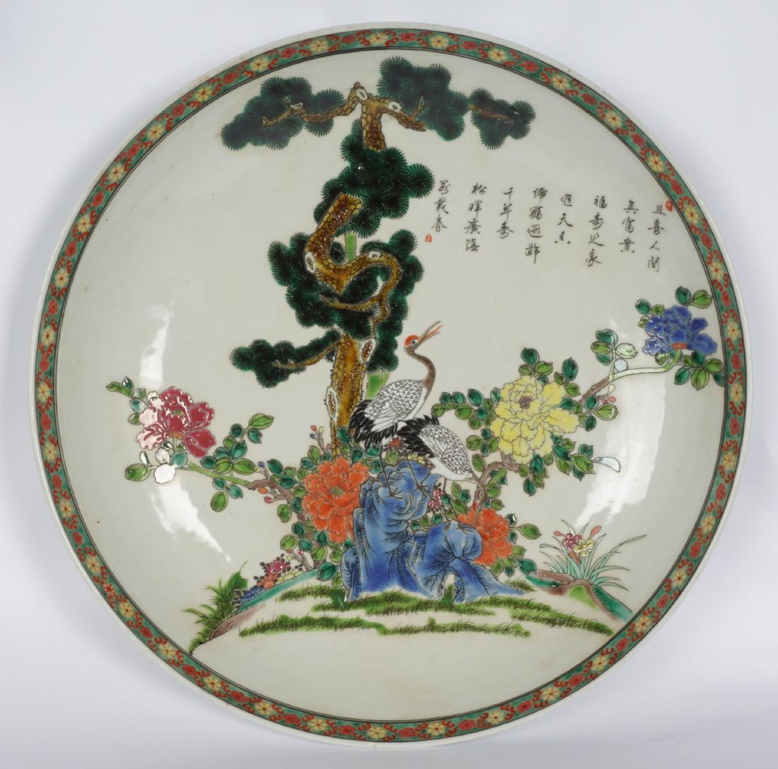 Large Chinese Polychrome Charger: Decorated with cranes, tree, blossoms and verses, floral rim, bearing a spurious Kangxi mark. 3'" h. x 15.75".