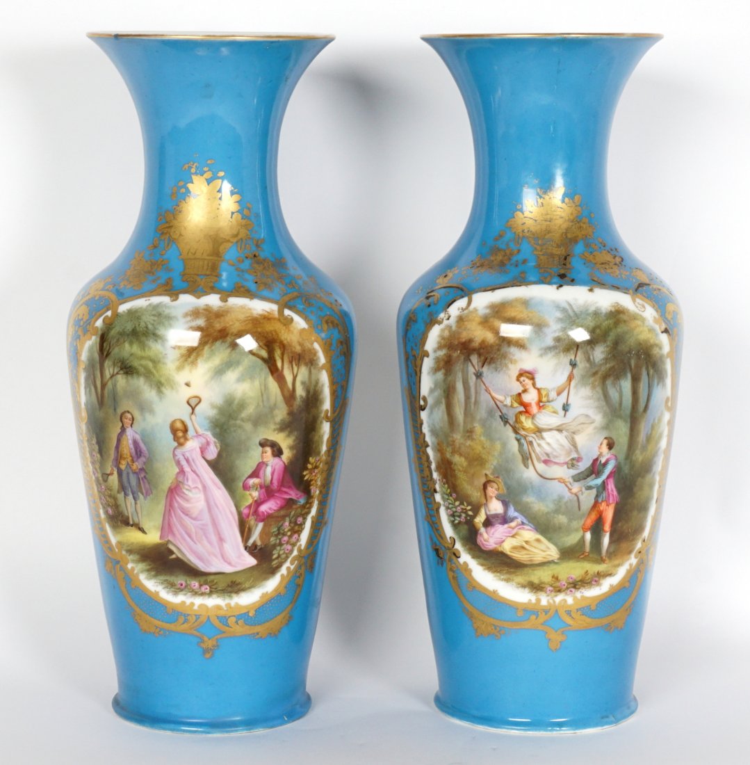 Pair Sevres Marked Hand Painted Vases: Turquoise blue ground with gilt accents, one with hand painted scene of people playing badminton, the other with women swinging, marked with blue Sevres mark on base, 19" h. x 8". Condition: One with