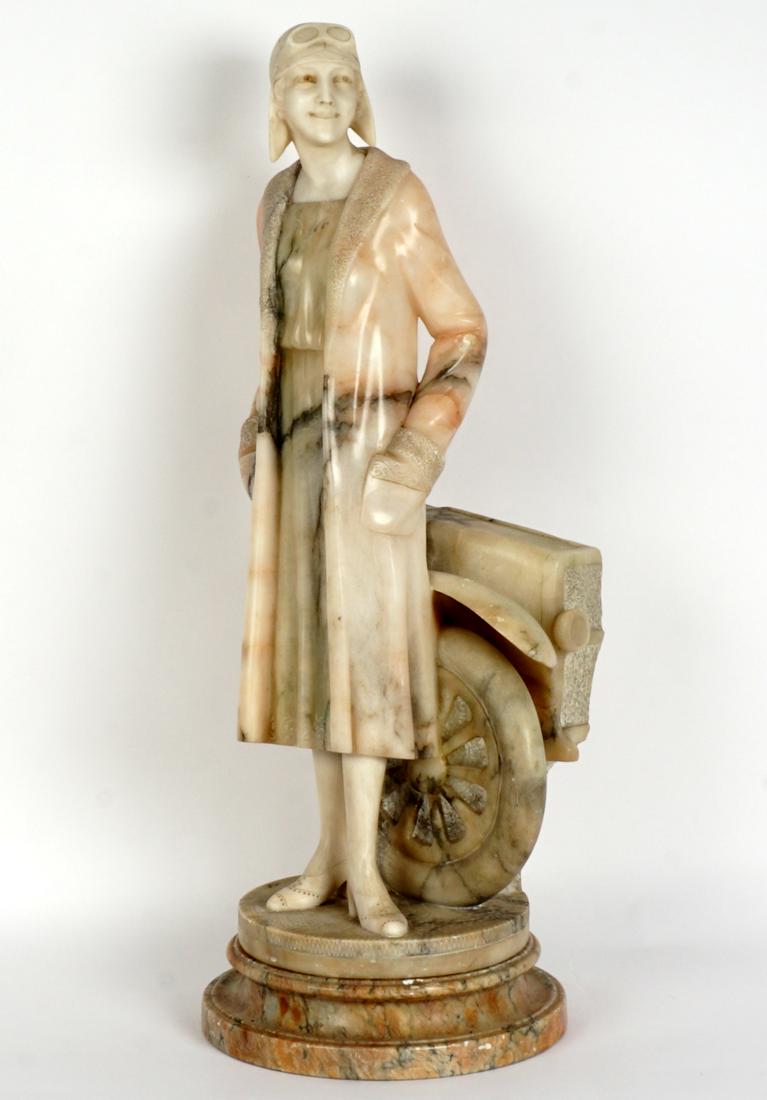 Italian Carved Alabaster Female Race Car Driver: Standing figure of an early 20th Century woman race car driver in front of a partial car. Illegibly marked on base, overall measures 24.75" h. x 9.25". Sold with a base, 2.25" h. x 9.75". Condition: C