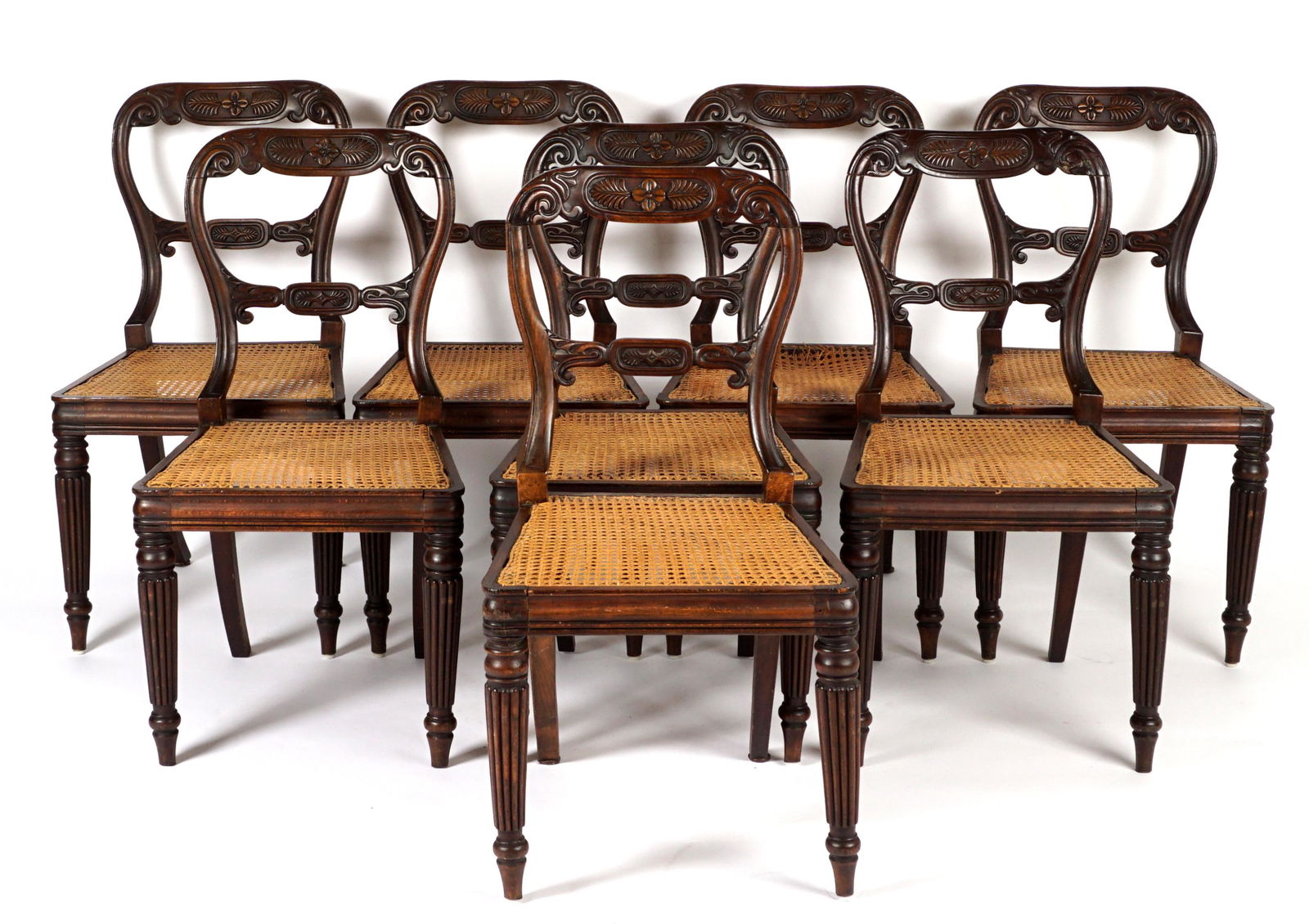 Set of Eight English Fruitwood William IV Chairs: Top rail and shaped back carved with foliate motifs, fluted front legs, saber back legs, caned seats, overall 33.25" h. x 20" x 18". Condition: One with breaks to caning at back of seat, other wear co