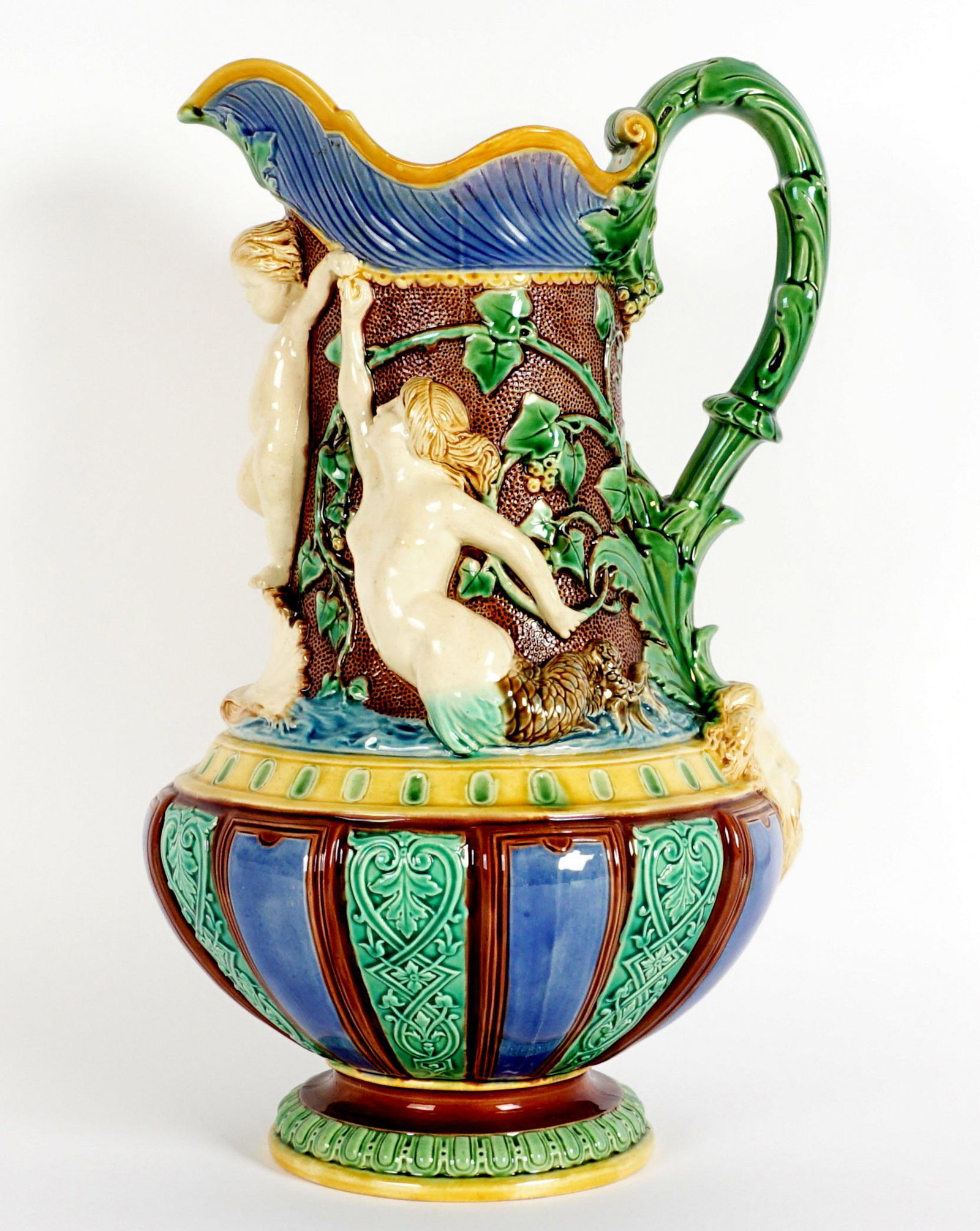 1862 Minton Neptune & Mermaids Majolica Pitcher: Majolica pitcher featuring mermaids, putti, and Neptune mask with foliate accents. Well marked on base with Minton, 474, and 1862 date mark. Overall 12.25" h. x 7.75". Condition: Lip glows under black