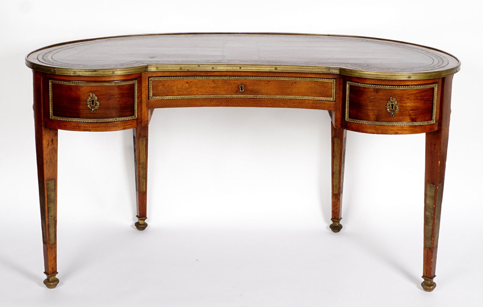 Leather Top Kidney Writing Desk: Kidney shaped body and inset embossed leather top, brass trim, 3 drawers, tapered legs with fluted brass panels, on brass feet, 29.75" h. x 55" x 28". Condition: Wear consistent with age and use.