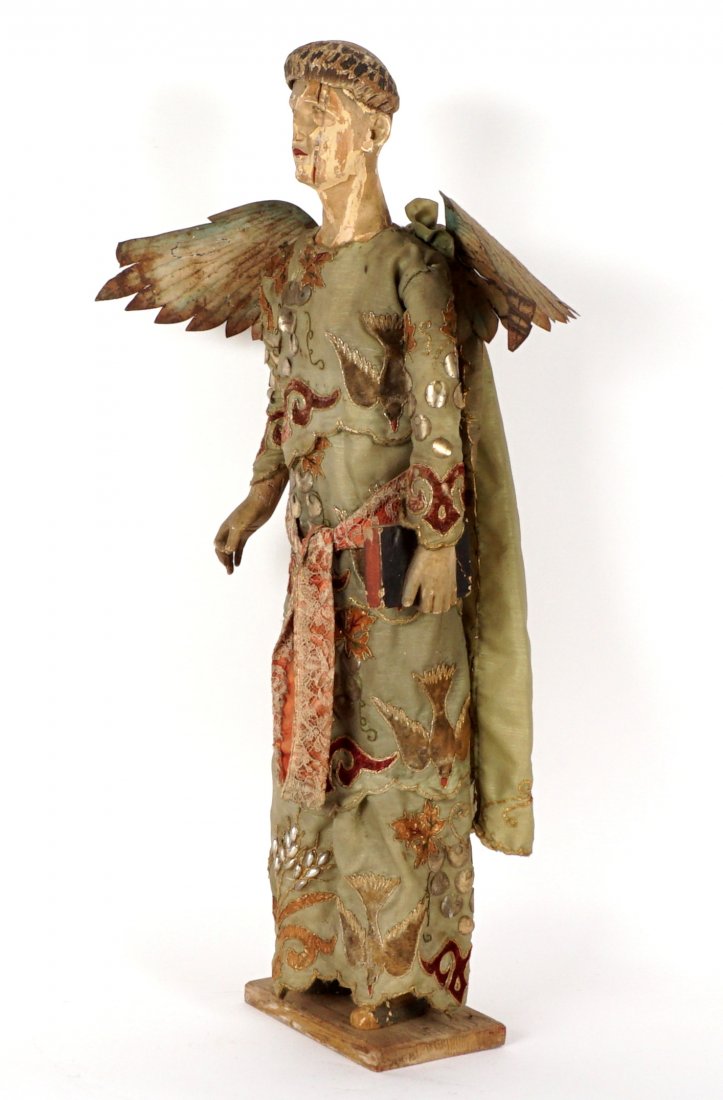 19th Century Carved Winged Santos Figure: Carved and polychrome paint decorated head and body, embroidered silk dress and cape with birds, an foliate motifs, applied metal beads and decoration. Painted metal wings, bible in one hand, affixed