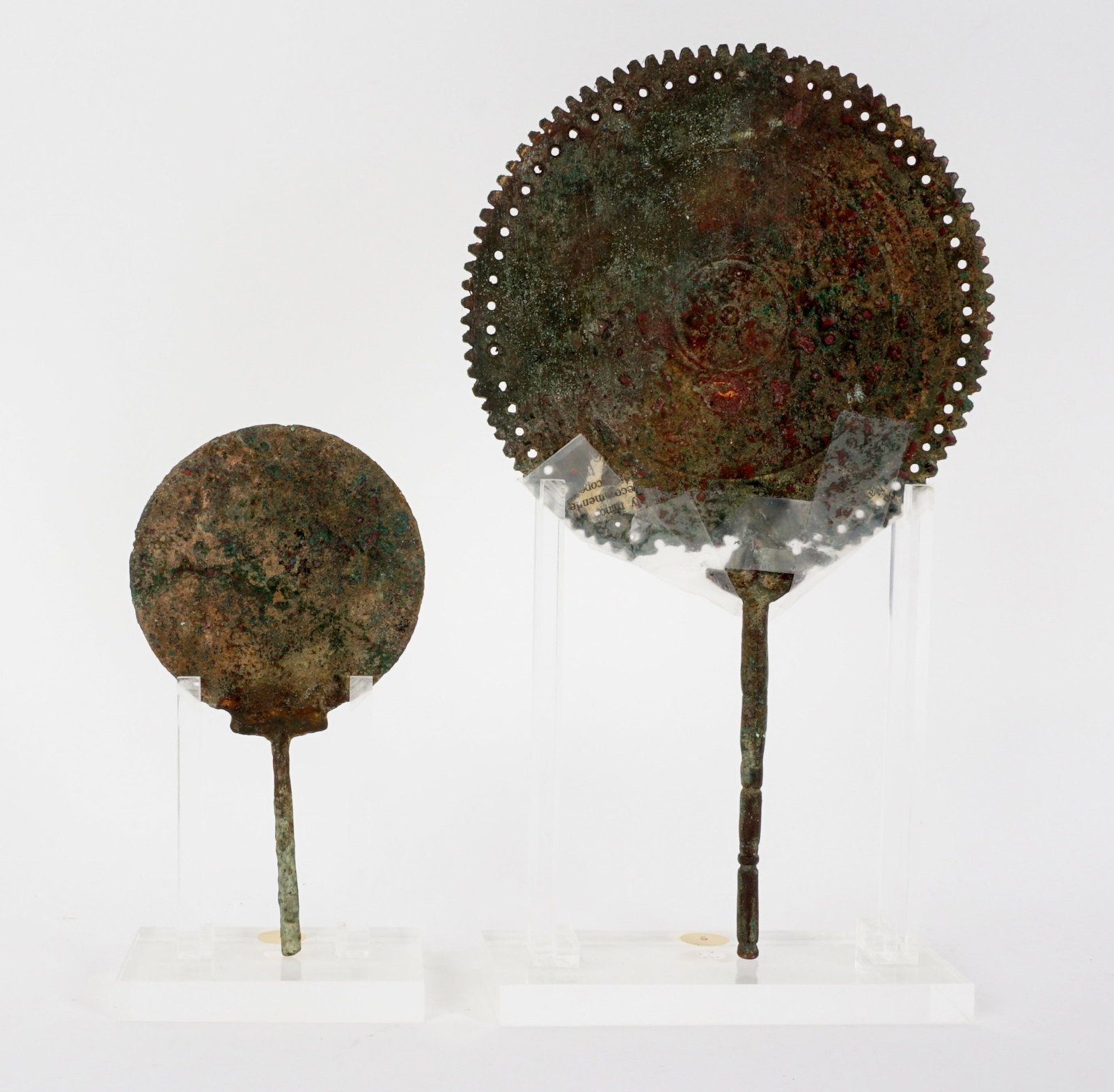 Two Roman Bronze 2nd C Bronze Mirrors: Two mirrors total, both 2nd Century, to include 1) Reticulated rim, remains of engraved design verso, overall 9.25" h. x 5.5". Handle has damage at joint, taped together. 2) Smaller mirror, 5.5" h. x
