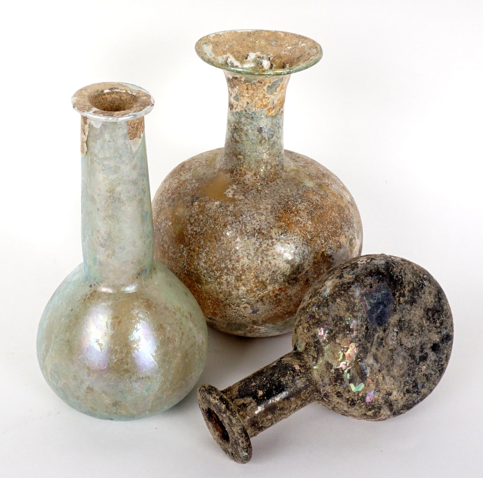 Three Piece 2nd C Roman Glass Bottles: Three iridescent glass pieces total, each dating from the 2nd Century. Bottle sizes 6" h. x 4.5", 6.5" x 3.25", 4.75" x 3". Condition: All three intact with no repairs noted under black light. Varying