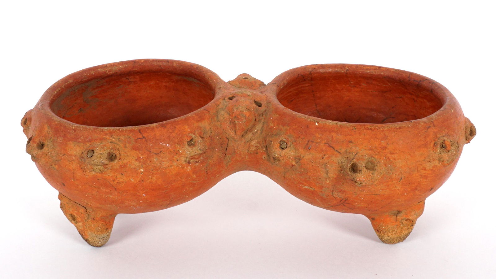 Pre-Columbian Redware Monkey Faces Double Bowl: Redware connected double bowl with band of monkey faces, two faces at joint, on four legs. 3" h. x 9".