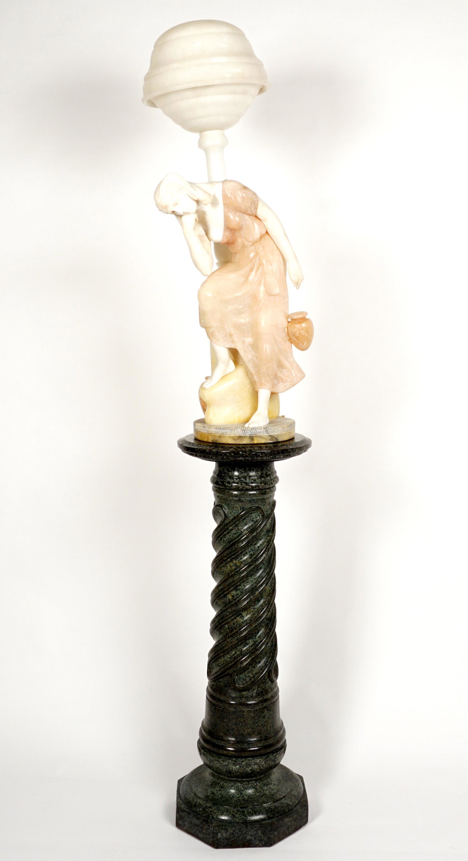 Italian Carved Alabaster Woman Fountain Lamp: Figural alabaster lamp featuring a seated woman waiting for a vessel to fill at a wall fountain, carved accents to skirt. No visible signature, missing fixture. Overall 44" h. x 13.5" x 10.5". Sold wi