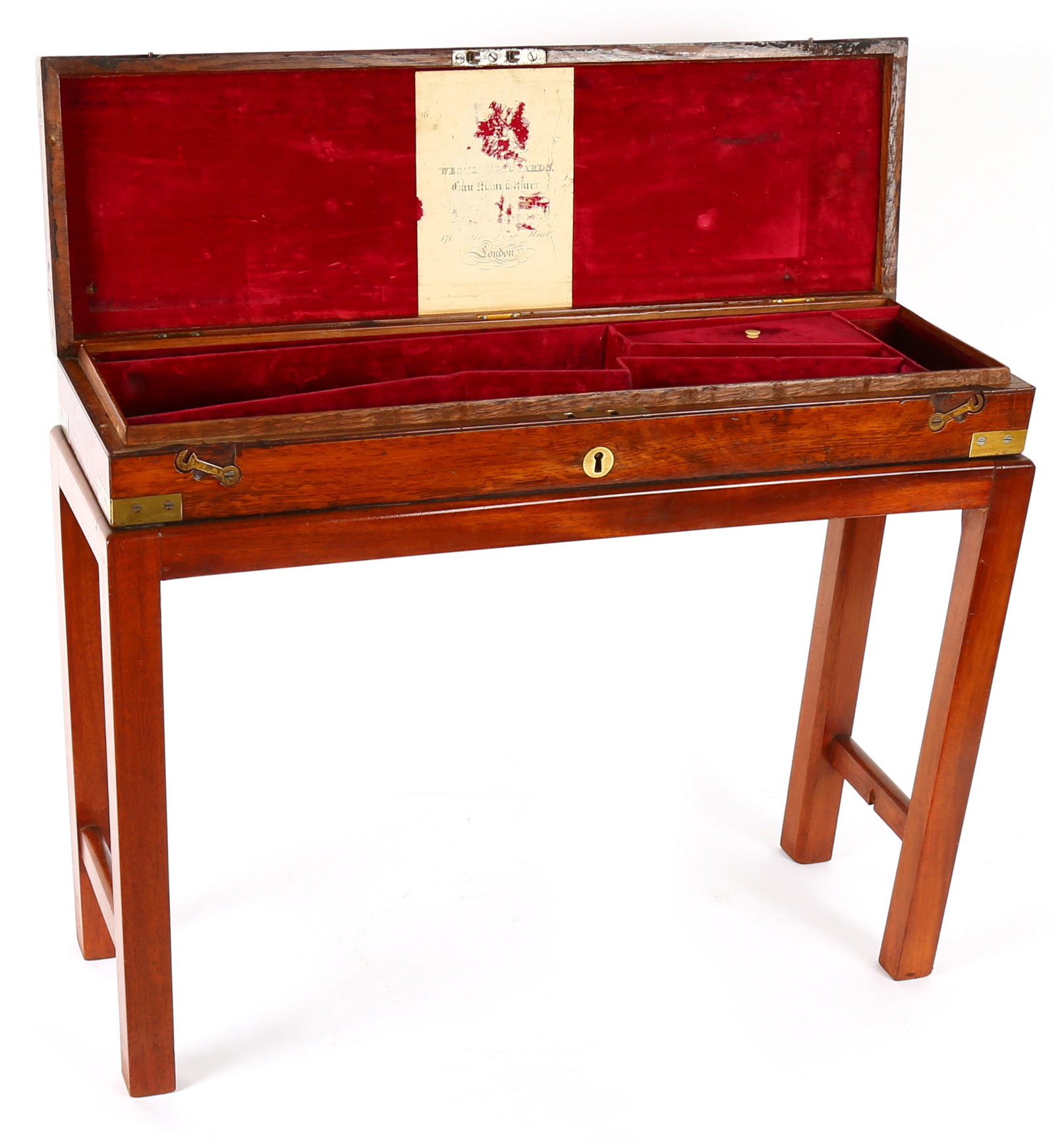 Westley Richards Walnut Gun Case on Stand: Walnut case with brass bullseye decoration on hinged lid, fitted felt interior, partial Westley Richards label remains. Affixed to stand, overall measures 19" h. x 24.5" x 8". Condition: Scratches and