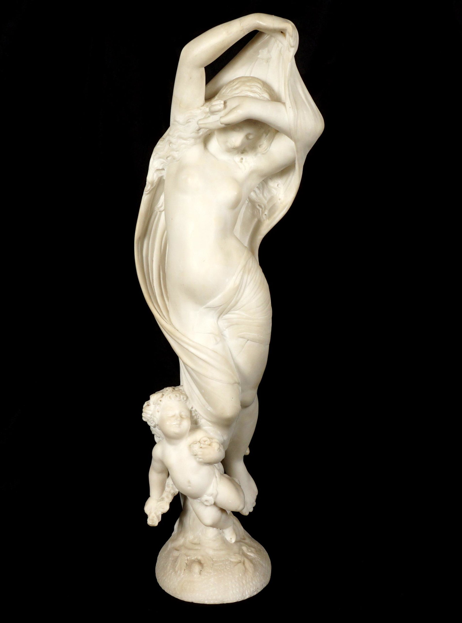 Carved Alabaster Semi Nude Maiden Sculpture: Carved alabaster figural semi nude maiden with putti at feet, no visible signature. Overall 28" h. x 6.5" x 10". Condition: Repair to arm, missing fingers, sold with all faults.