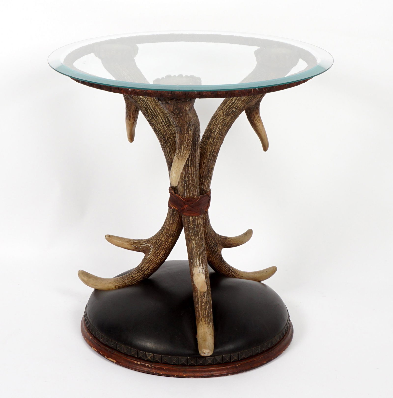 Faux Antler Glass Top Side Table: Round glass top over composite elk antler support, padded leather base, overall 26" h. x 24". Condition: Multiple chips to glass edge.