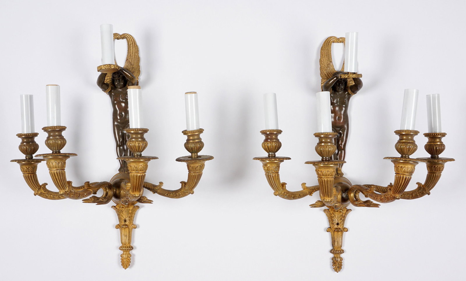 Pair Figural Winged Angel Bronze Wall Sconces: Patinated bronze figure of winged angel holding a light, four arms with stork heads, lower urn finial, overall 18.75" h. x 14.5" x 9.25".