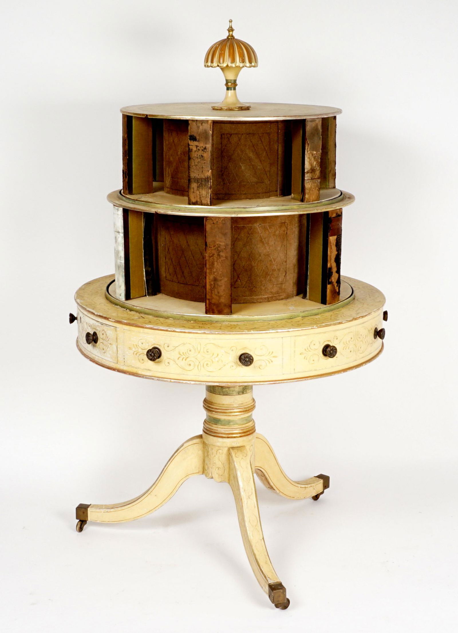 Edwardian Two-Tier Lazy Susan Library Table: Paint decorated all over, umbrella finial over two separately rotating lazy susan book shelves over single drawer drum table base. Turned pedestal, three splayed legs ending in castors