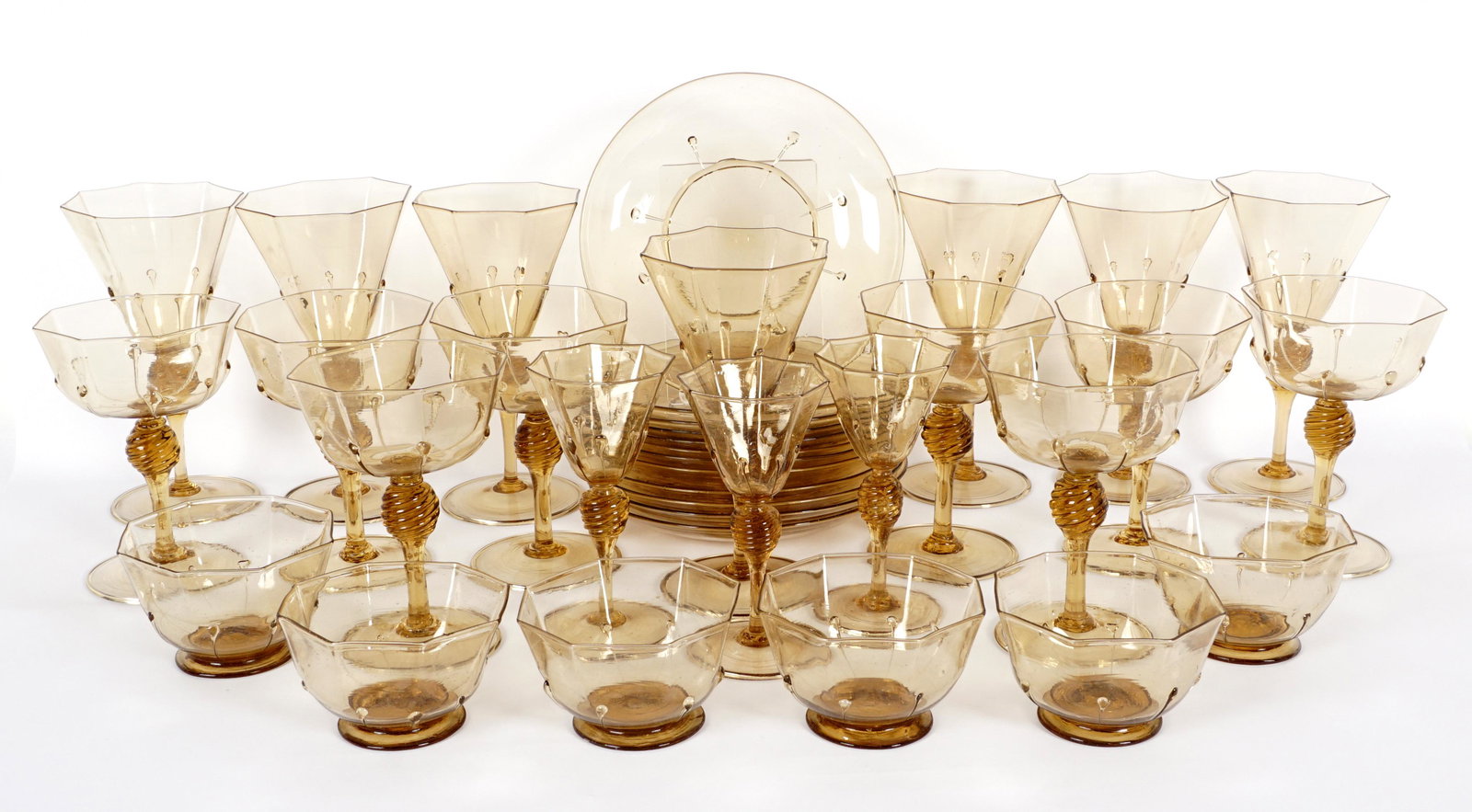 35 Piece MVM Cappellin Amber Glass Stems & Plates: Approx. 35 pieces total by noted Murano glass maker MVM Cappellin to include 7 wine glasses (7.25"), 8 champagne / sherbet (5.5"), 3 cordials (5.5"), 11 plates (7.25"), 6 bowls (2.25"). Condition: Sta