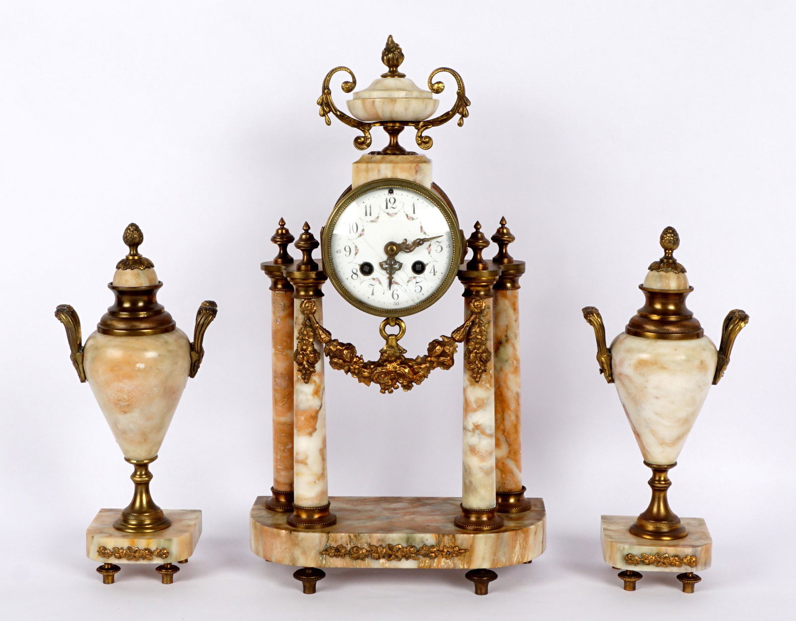 Three Piece French Marble Clock Garniture Set: Three pieces total, marble portico clock with urn finial, gild bronze accent swag, hand painted porcelain dial. French time and strike movement stamped JUST, overall 16.5" x 9.25' x 4". Sold with matc
