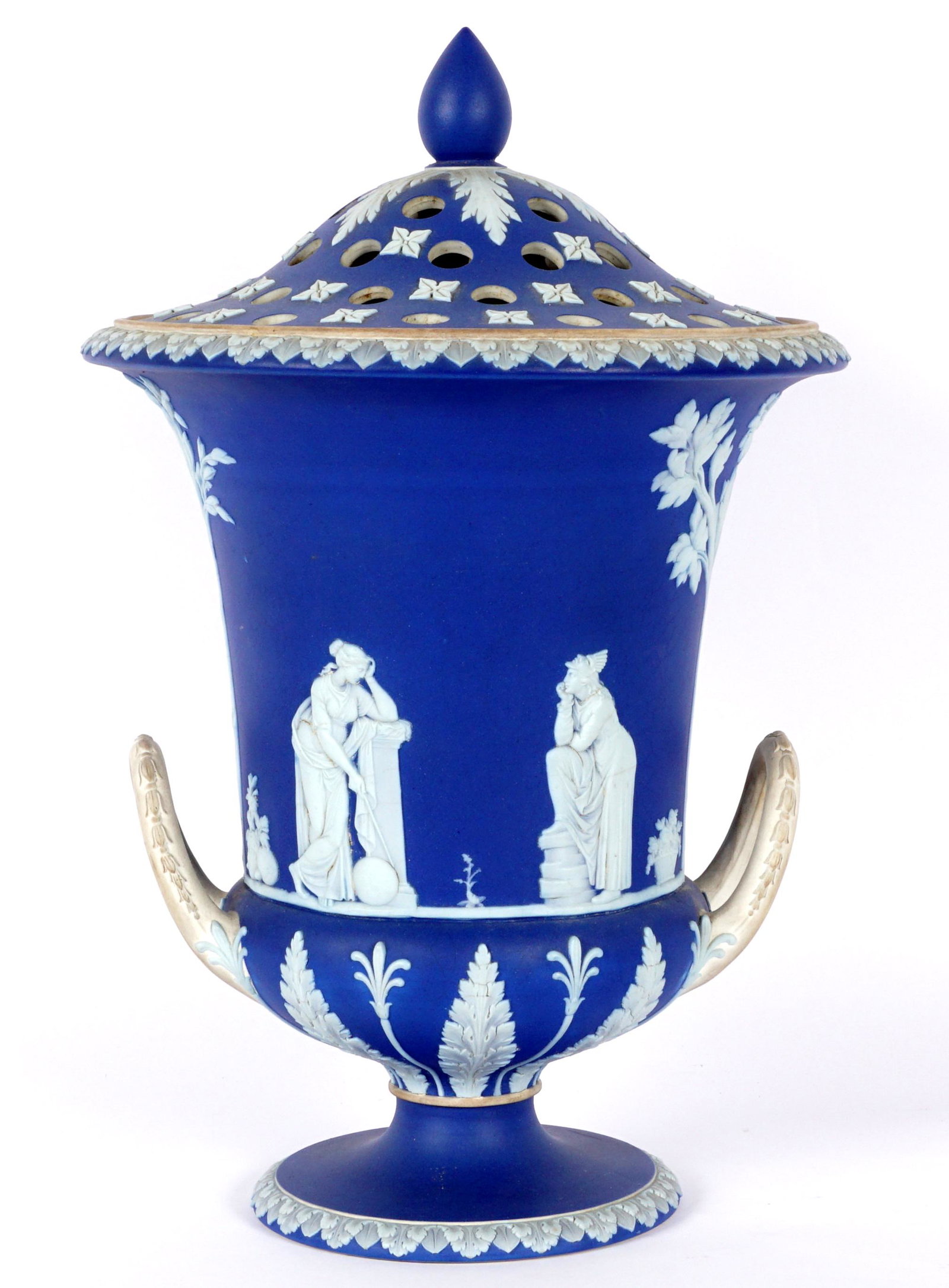 Large Wedgwood Jasperware Flower Urn: Dark blue with cream handles, white neoclassical decoration, pierced flower frog lid, stamped Wedgwood on foot, 15.5" h. x 10". Condition: Crack at rim and on foot, ground chip repair on rim.