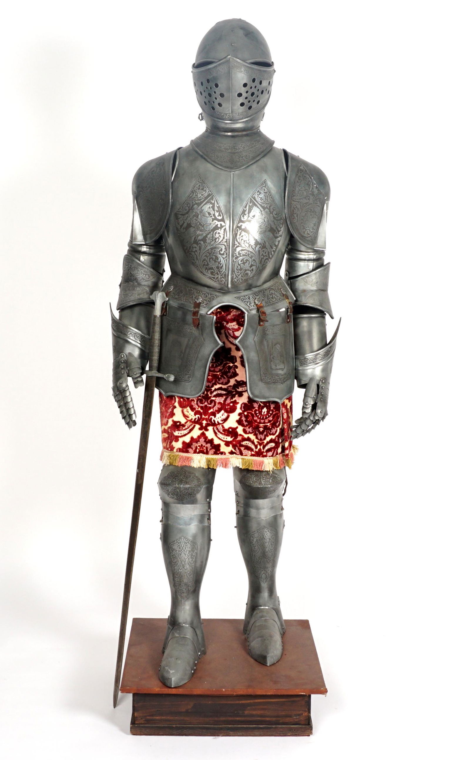 20th Century Suit of Armor: Decorative metal suit of armor with cloth apron, engraved jousting scenes on breast plate, foliate scroll panels, on wood form, armor measures 69" h. x 24" x 20". affixed to wood base, 6" h. x 21.5" x