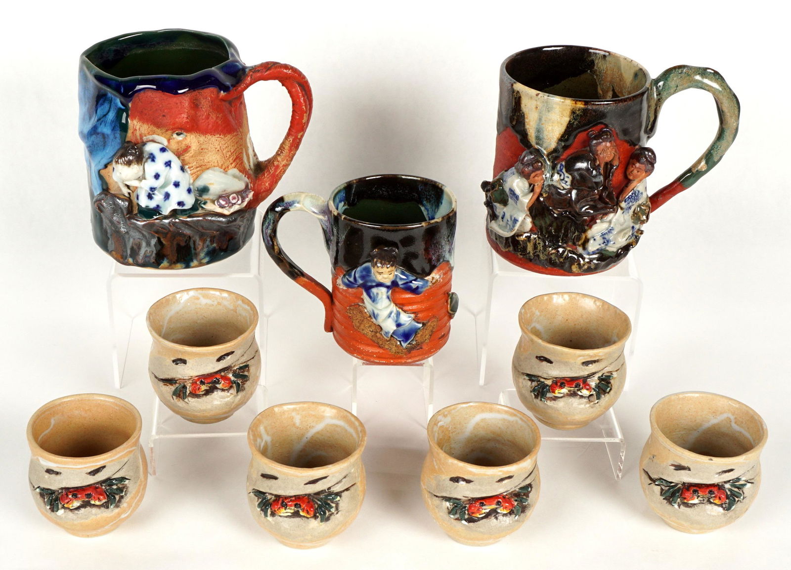 Nine Piece Japanese Sumida Gawa Mugs and Cups: Nine pieces total to include 1) Mug with See no evil, hear no evil, speak no evil women, signed on plaque, 5" h. x 6". 2) Mug with girl looking over cliff, signed on plaque, 5" h. x 6.25". 3) Small mu