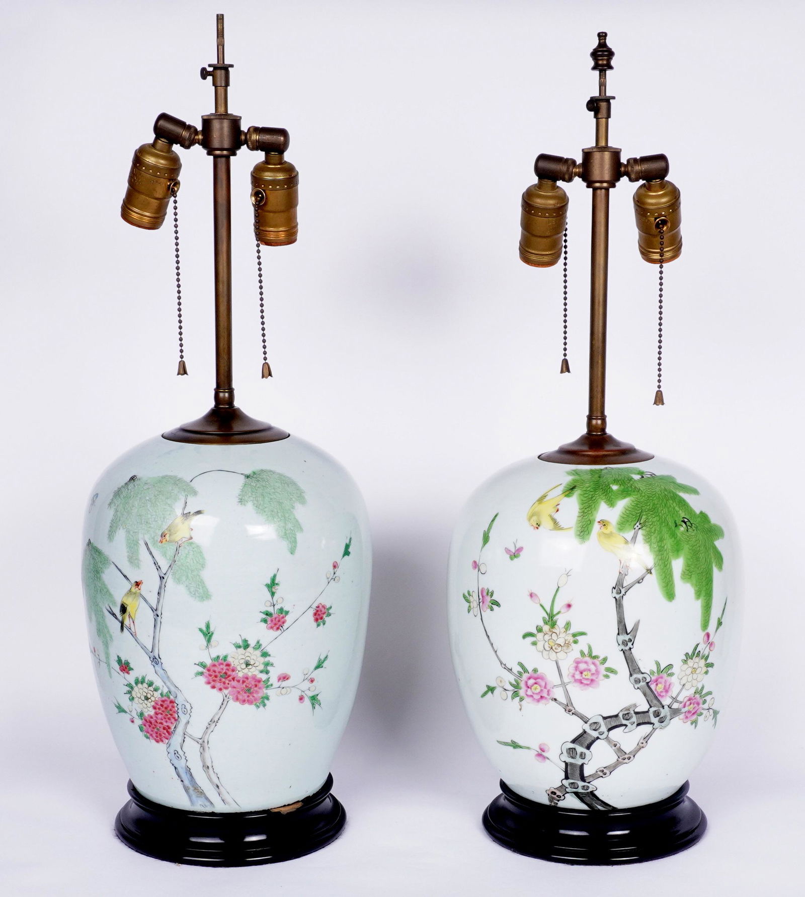 Pair Chinese Famille Rose Jars Mounted as Lamps: Ovoid form porcelain vase with birds and branches enamel decoration, ebonized turned wood base, double socket fixture, no shades or finials. Overall 24" h. x 8". Condition: Chips to base.