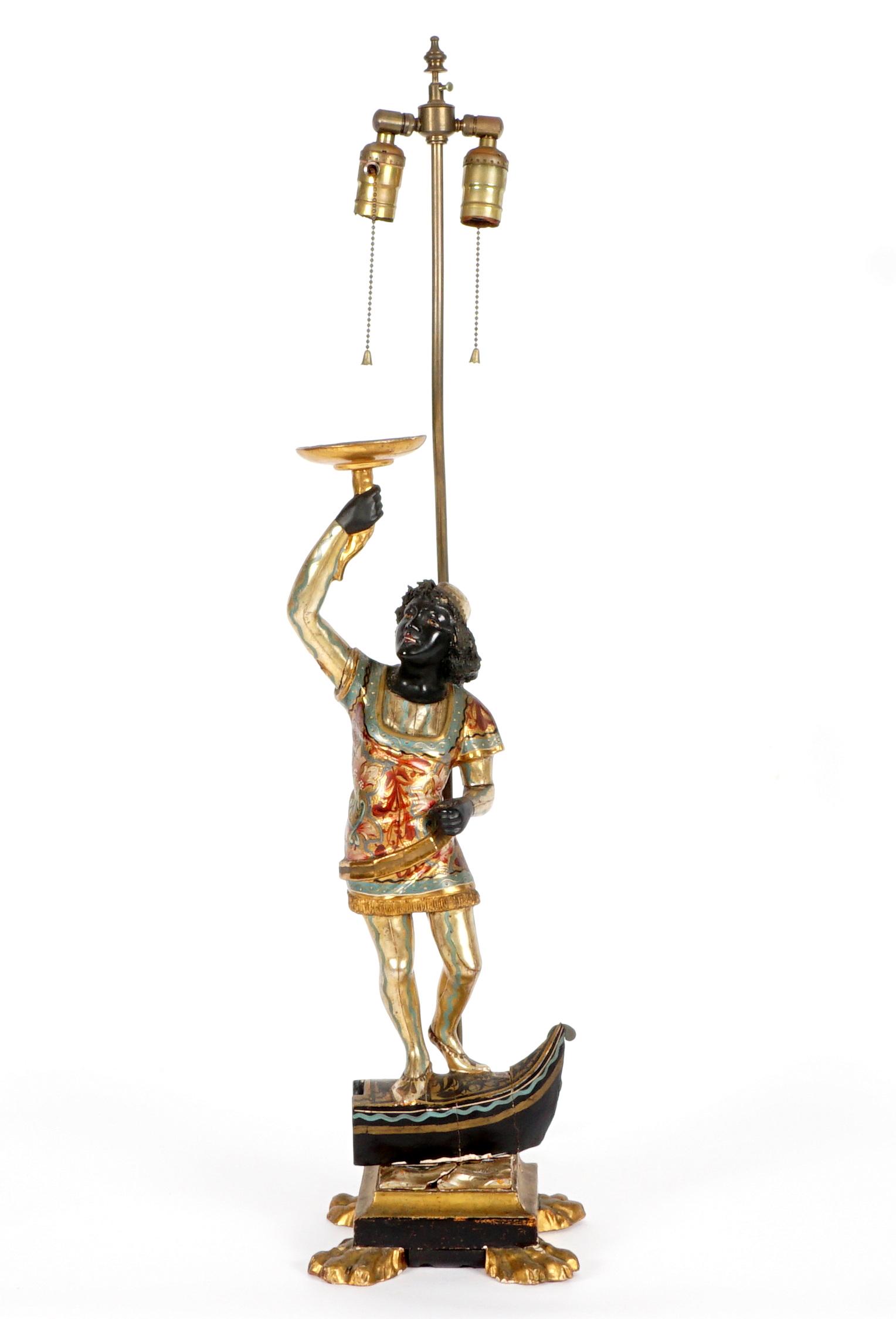 Antique Venetian Carved Blackamoor Gondolier Lamp: Carved wood gilt and polychrome paint decorated figure of a blackamoor standing on a gondola, holding a torch, Carved wood base with four paw feet. Double socket fixture, overall 36.75" h .x 8" x 8.25