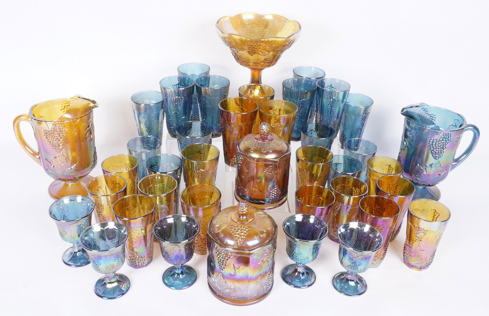 40 Piece Grape Vine Carnival Glass: 40 pieces total in marigold and blue/purple to include 29 tumblers (5.75" h.), 5 wine glasses (5.25"), 2 covered jars (larger 8.25" h.) 2 pitchers (10.25" h.), compote (8.5" h.).