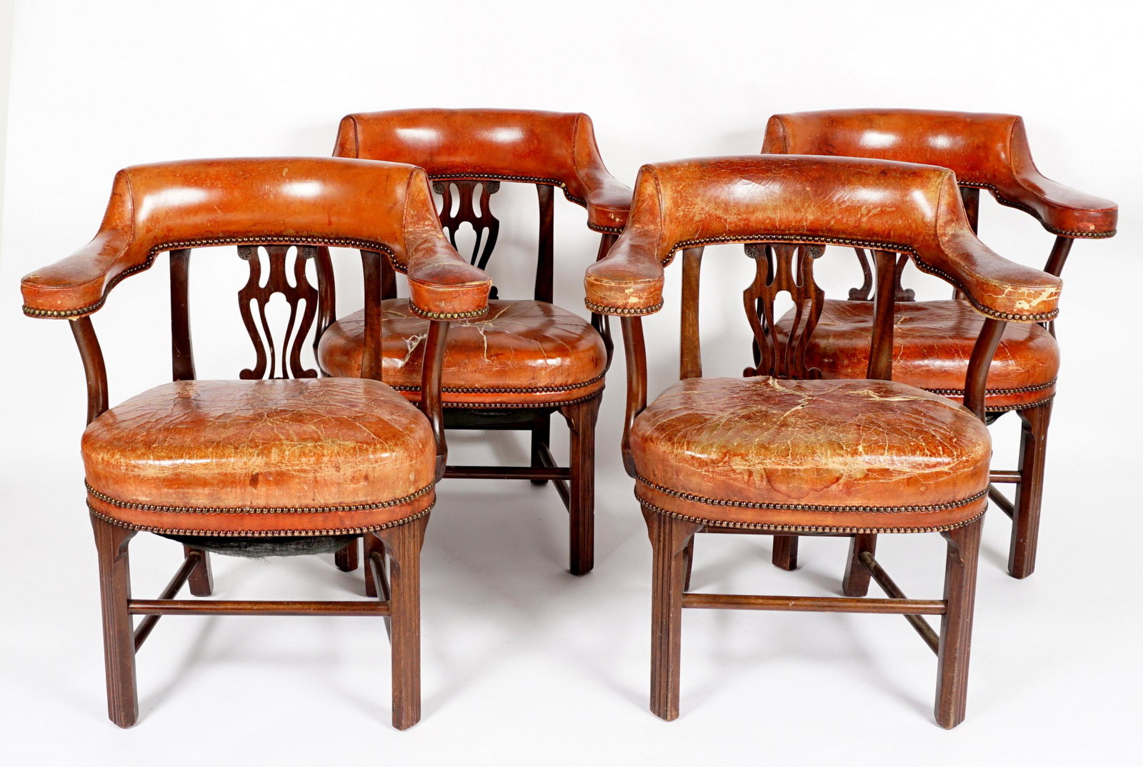 Four Georgian Style English Leather Library Chairs: Circa 1910, barrel back, lyre form back splat, tacked brown leather upholstery, canted fluted front legs, overall 34" h. x 29.5" x 22.5". Condition: Extensive cracking to leather, other wear consisten