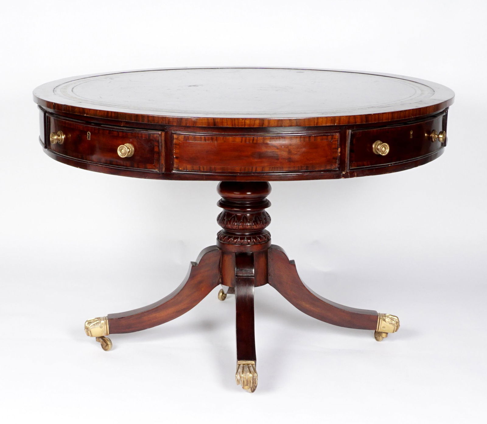20th Century Georgian Style Drum Table: Embossed inset leather mahogany top, skirt with 4 drawers, carved and turned pedestal support, splayed legs ending in brass feet on castors. Overall 28.5" x 43.5". Condition: Chips, gouges, and scratc