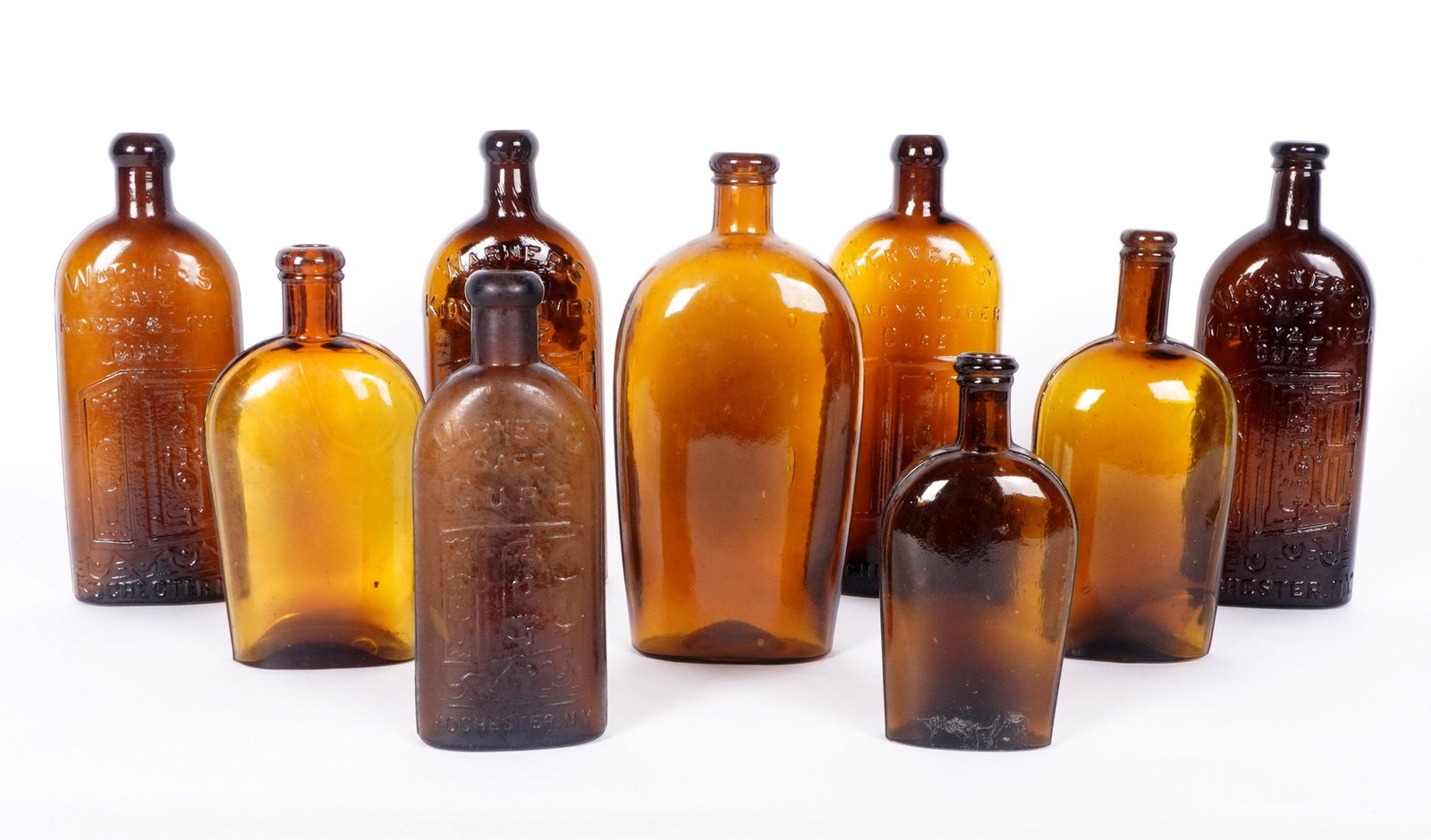 9 Antique Amber Bottles Warners Safe Kidney & More: Nine amber glass bottles to include 4 Warner's Safe Kidney & Liver Cure, Rochester New York, 9.5" h.. Another Warner's bottle, 7.5" h.; 4 other unmarked bottles, tallest 9" h.