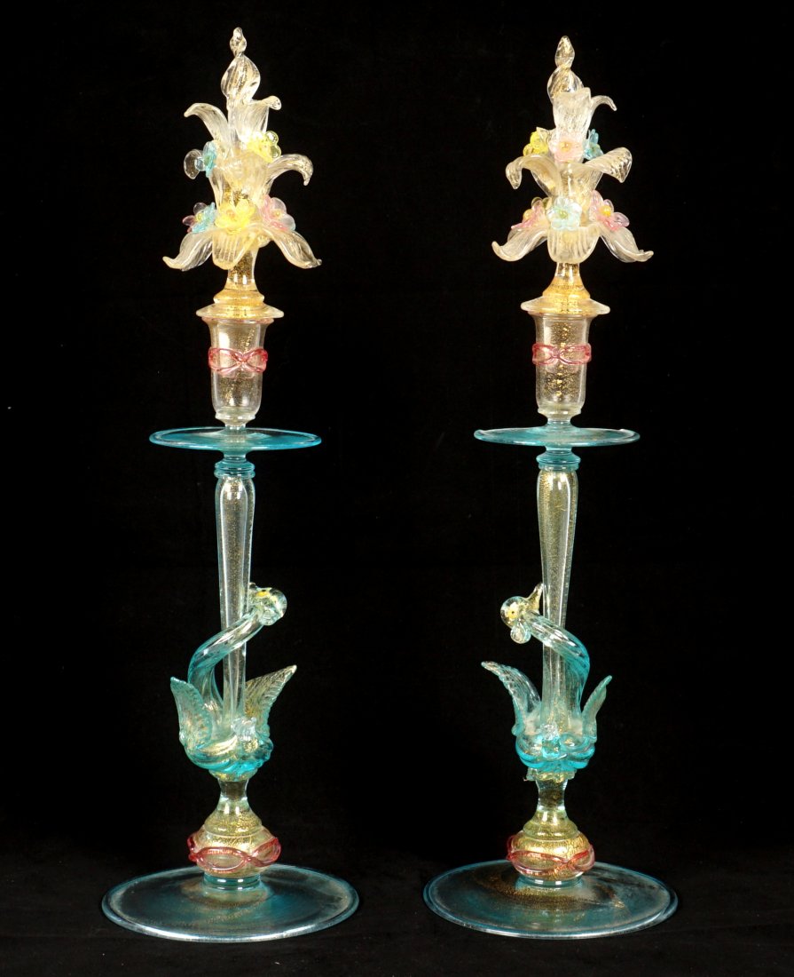 Pair Murano Glass Figural Swan Candlesticks: Pair polychrome Murano glass candlestick with foliate and floral motif finials, figural swans on shaft, overall 20" h. x 5.75" base dia. Condition: One with loss to bobeche and finial, both with chips