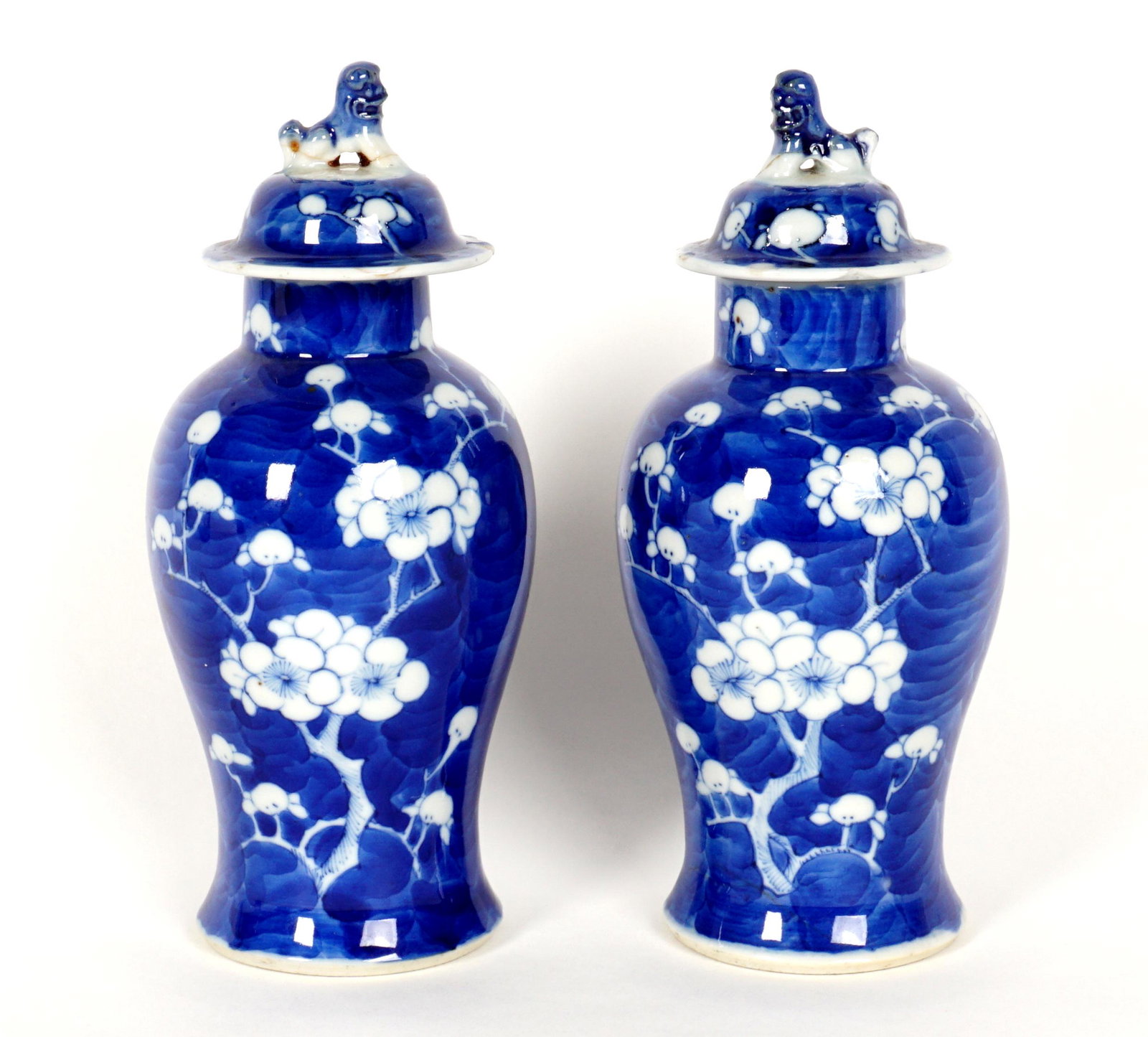 Pair Chinese Blue & White Decorated Covered Jars: Diminutive baluster form blue and white floral decorated, foo dog finials to lids , bearing a four character Kangxi mark. Overall 7" h. x 3". Condition: Both lids with chips and repairs to foo dogs, o