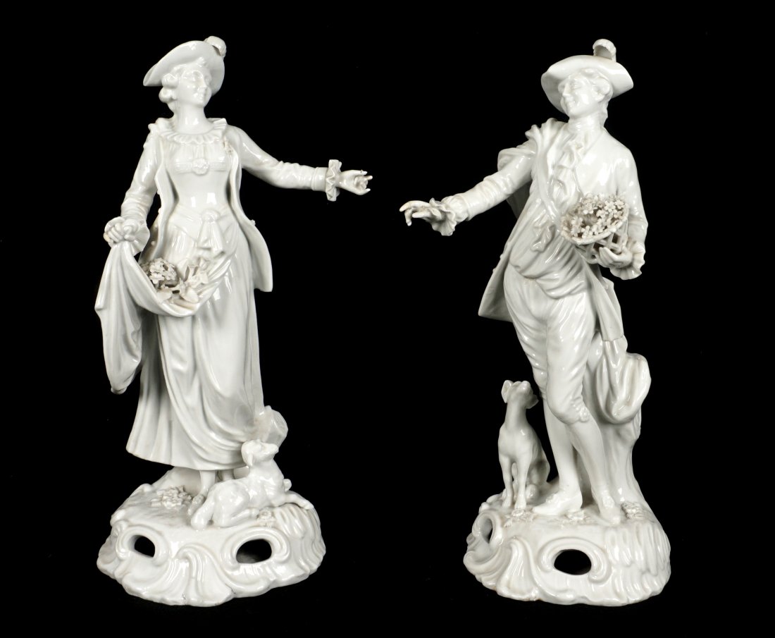 Pr Royal Vienna Blanc de Chine Porcelain Figures: Pair of man and woman, the man is holding a basket of flowers with a dog by his side, the woman with flowers in her dress and lamb at her feet. Both bearing the blue beehive underglaze mark, man measu