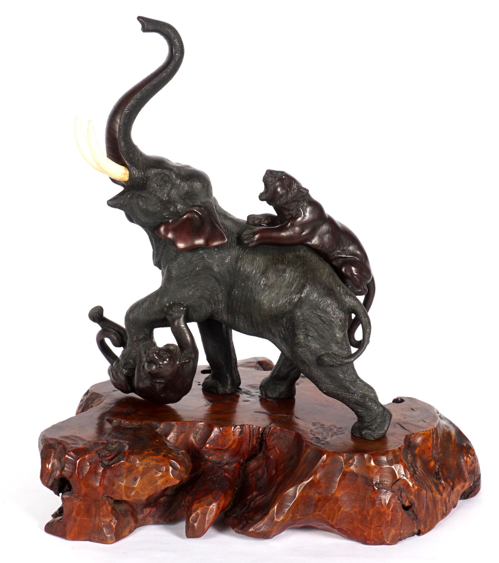 Meiji Period Bronze Elephant Attacked by Lions: Japanese Meiji period bronze figural group of an elephant being attacked by two lions, singed on belly. Overall 15" h. x 13.25" x 7". Sold with figured burl root stand 3.25" h. x 17" x 12". Condition:
