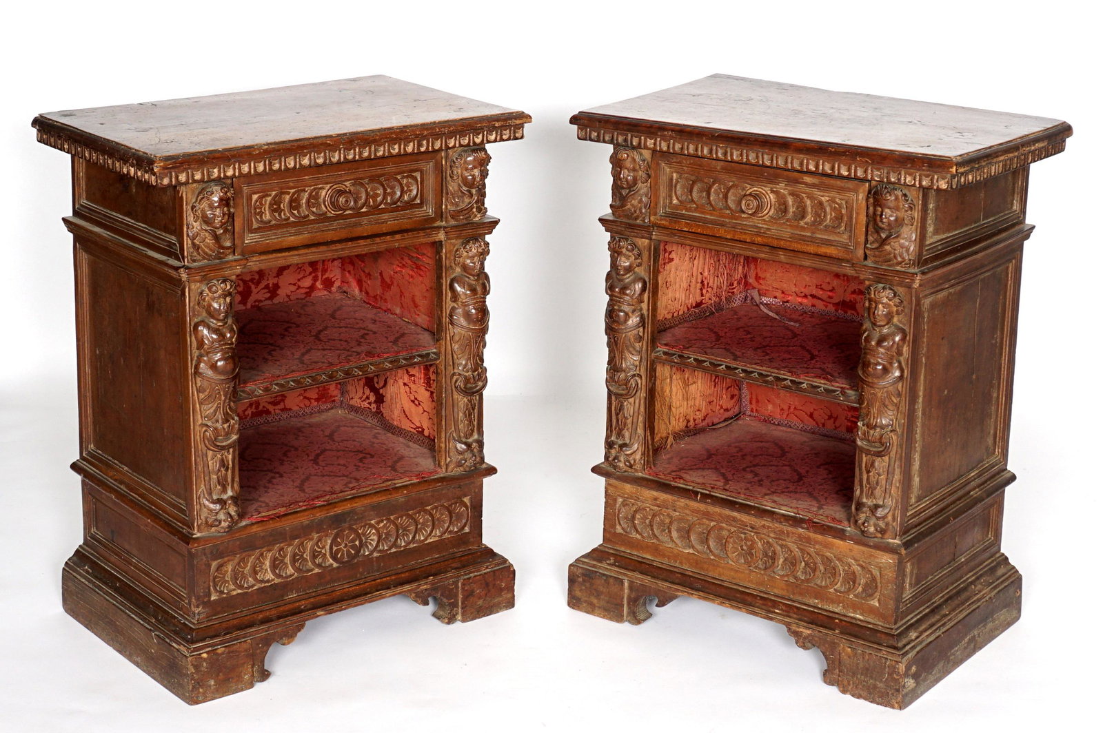 Pair Italian 17th/18th C. Carved Bedside Commodes: Renaissance revival carve walnut cases with figural putti masks and maiden bust stiles. Single center drawer over two open shelves, floral silk lined. Overall 33.5" h. x 26" x 17". Condition: Splits a