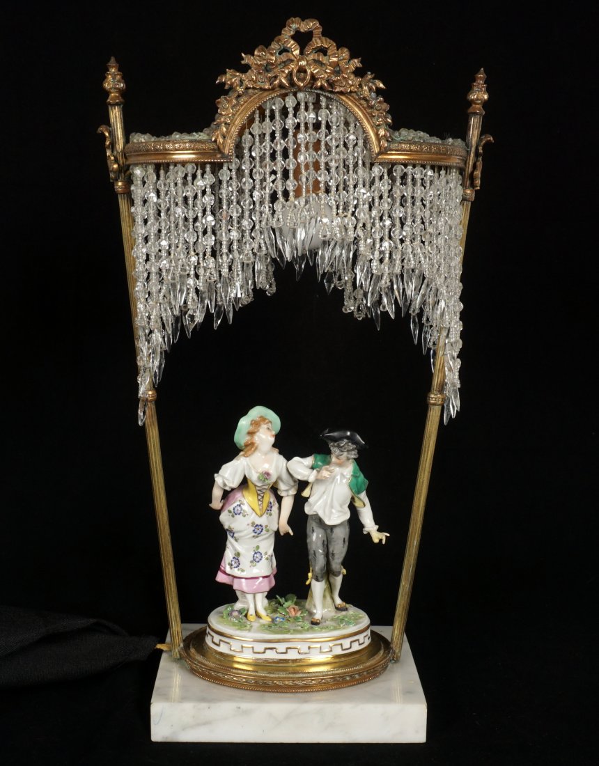 Beaded and Porcelain Figural Group Lamp: Brass canopy with beaded glass accents and drops, center porcelain figural group of man and woman, marble base, overall 15" h. x 9" x 4". Condition: Repair to hand on man.