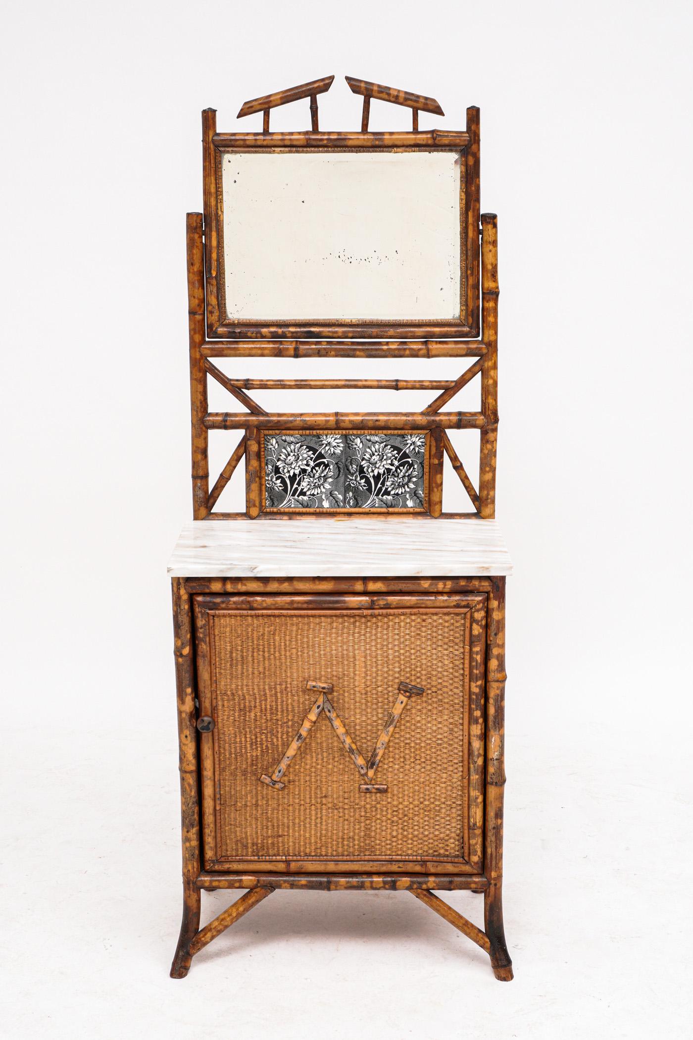 19th Century English Bamboo Side Dressing Cabinet: Architectural crest over beveled mirror, open work back splash, two floral porcelain tiles. Marble top over single door, "N" bamboo monogram, splayed legs. Overall 61.25" h. x 22.5" x 14". Condition: