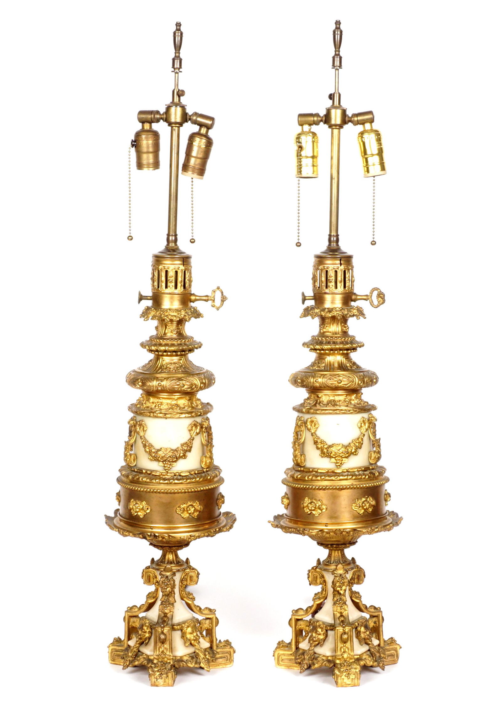 Pair French Gilt Bronze and Marble Table Lamps: Pair ornate gilt bronze decorated table lamps with marble interior components. Bronze decoration to include floral garland, foliate scroll, lion masquerons, all on three feet. Double socket fixture, o