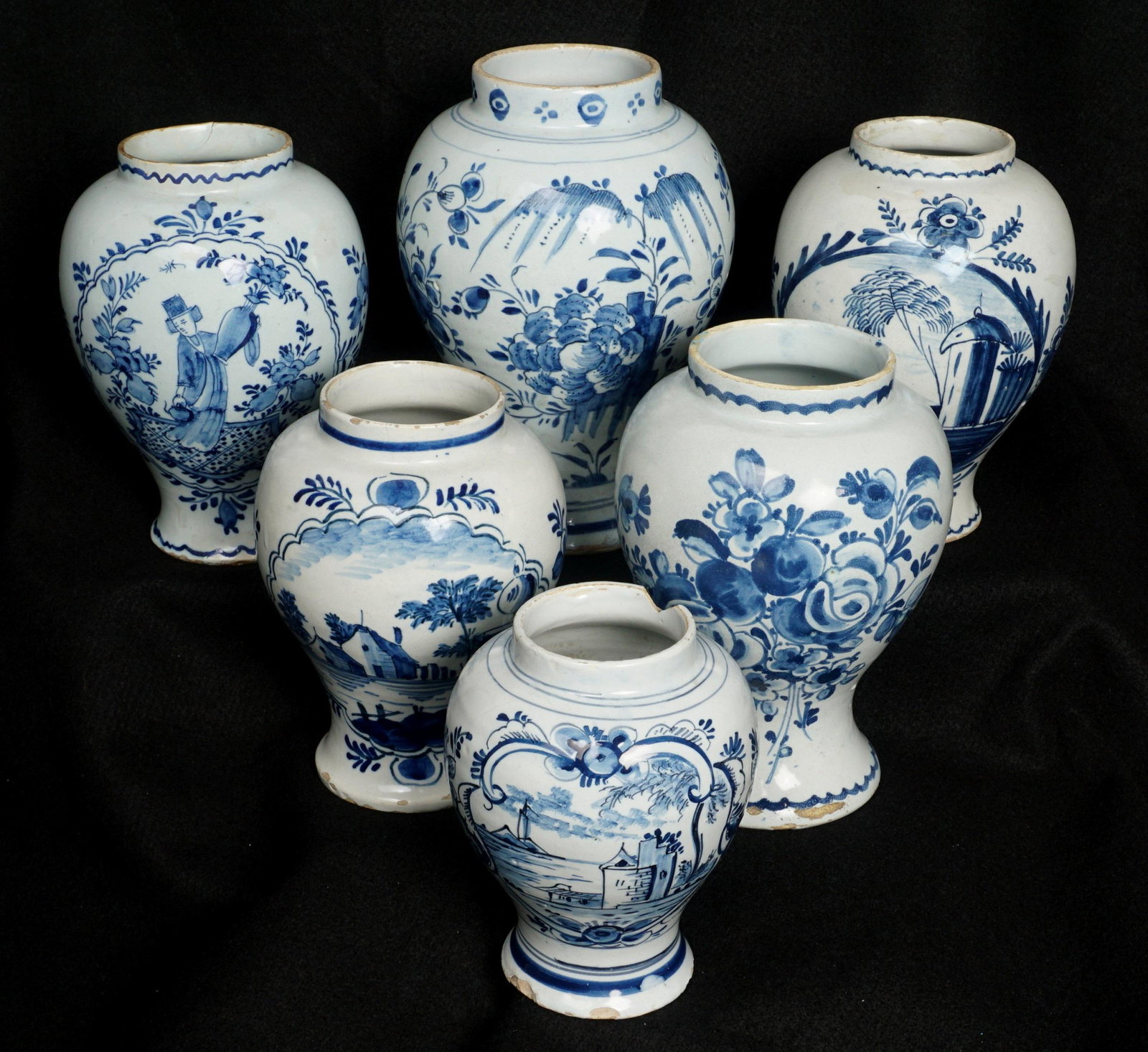 Six Delft Blue Jars: An assembled collection of six pieces total, each decorated with assorted genre scenes, foliate, and floral decoration, largest 8.5" h .x 5.75". Condition: Chips, cracks, crazing, and repairs to be ex