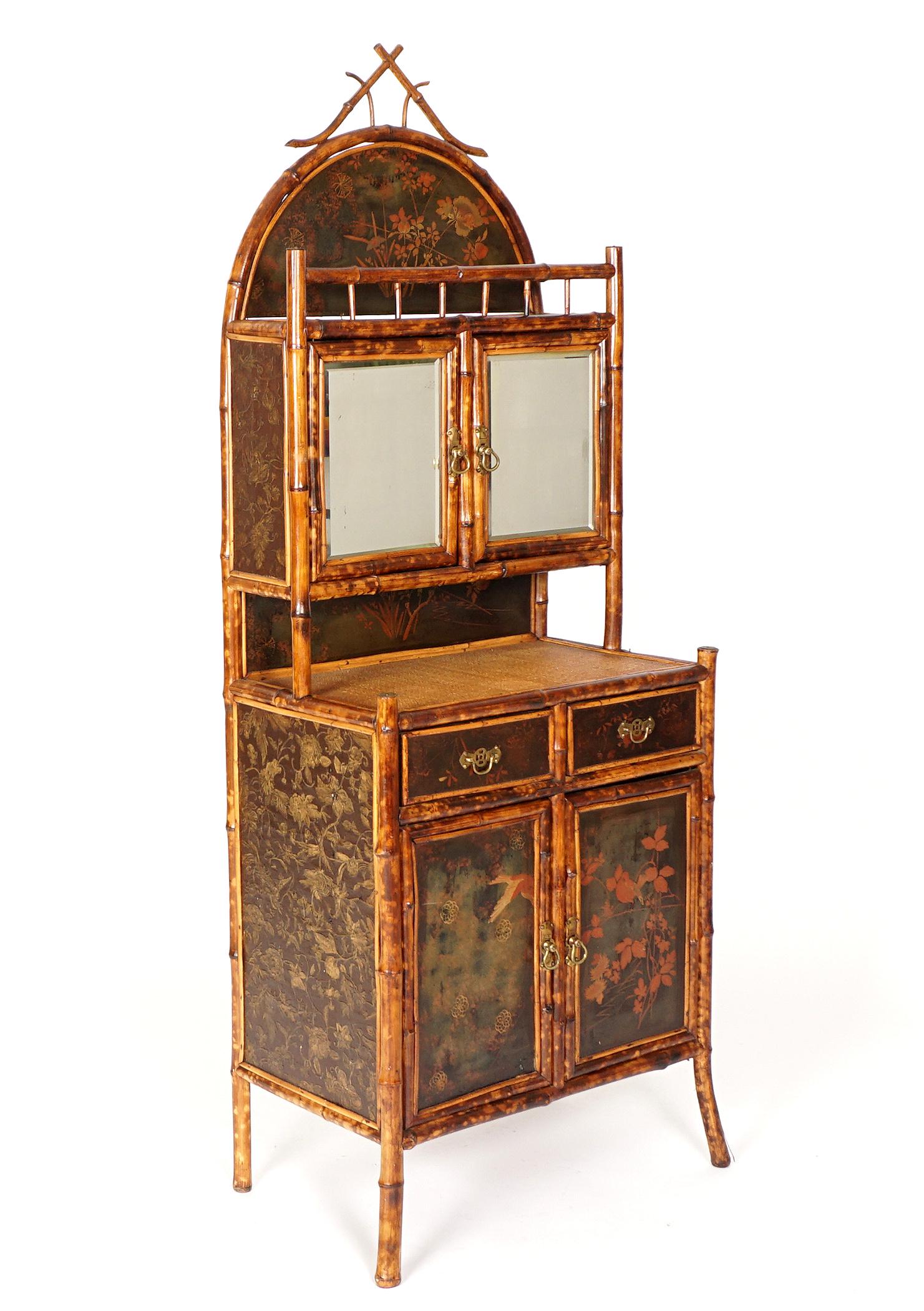 Victorian Bamboo and Chinoiserie Decorated Cabinet: Arched crest chinoiserie paint decorated floral motif panel, bamboo front gallery, two mirrored doors. Base with woven top over two drawers over two doors, all with paint decoration. Sides with raised