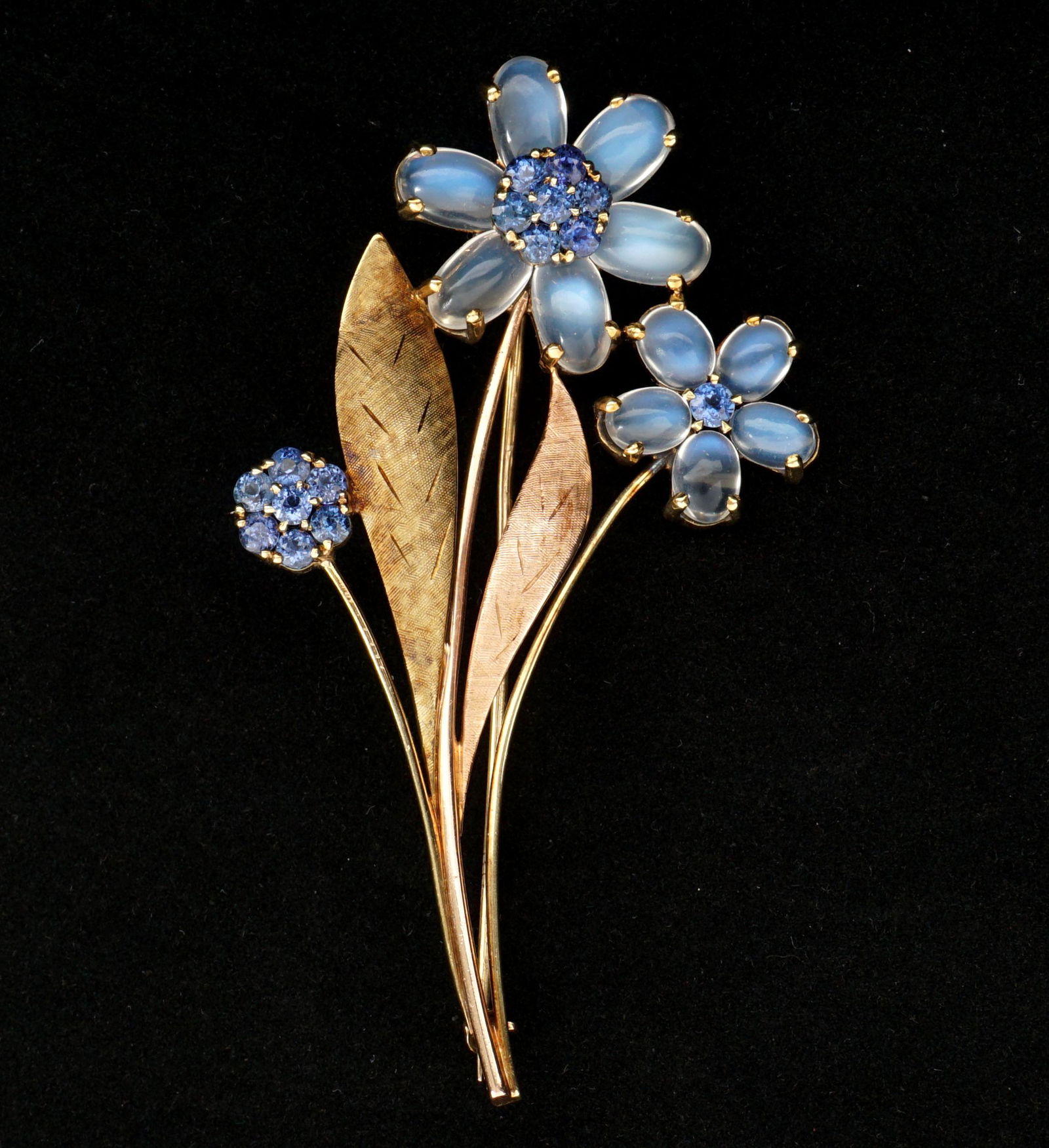 14k Gold Sapphire and Moonstone Floriform Brooch: 14k yellow gold brooch / pin, leaves and flowers design, 15 round cut accent sapphires, 11 moonstone petals, 2 7/8" x 1 5/8". Approx. 15 grams inclusive.